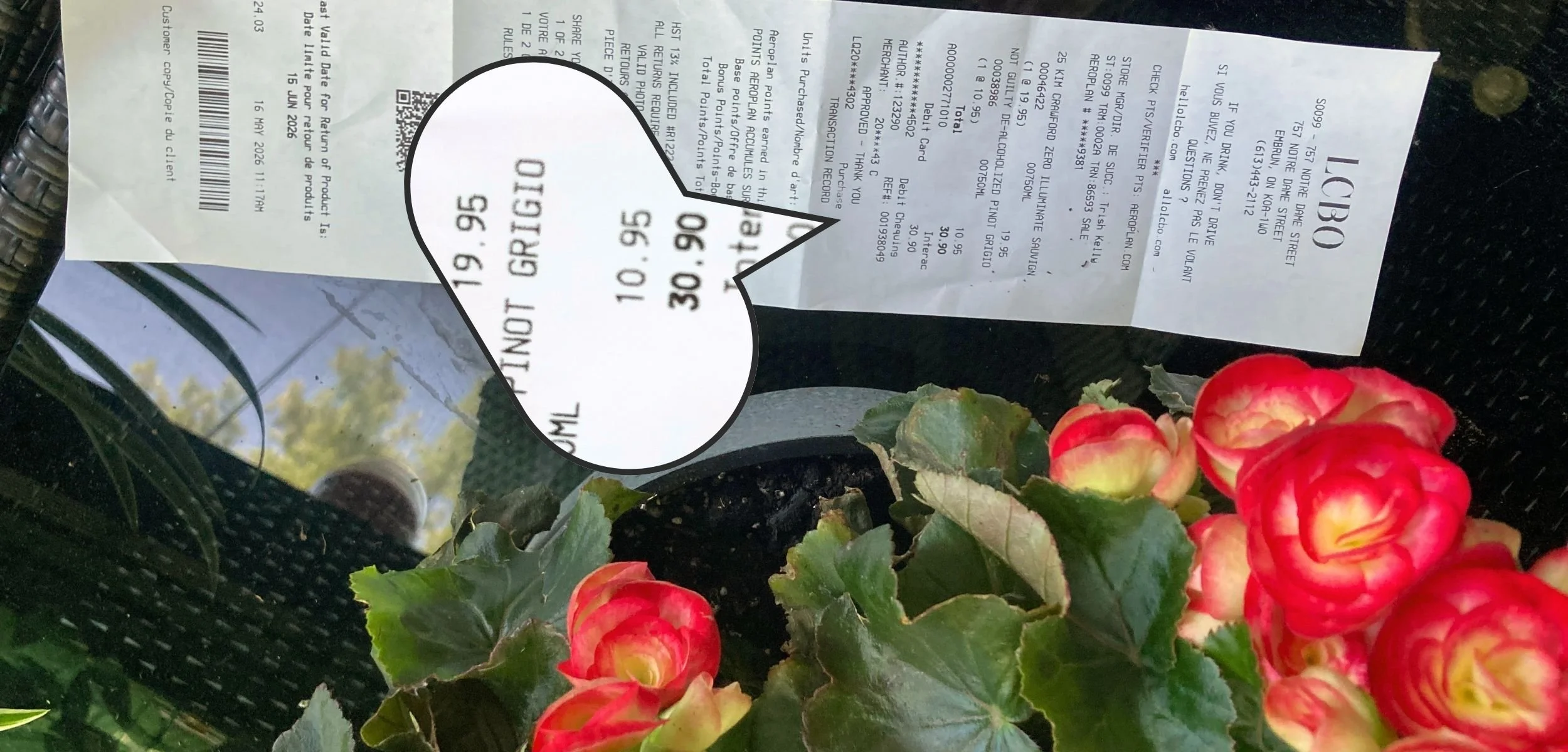 A close-up of a receipt from LCBO showing prices for non-alcoholic wine and a flower pot with red begonias on a black surface.