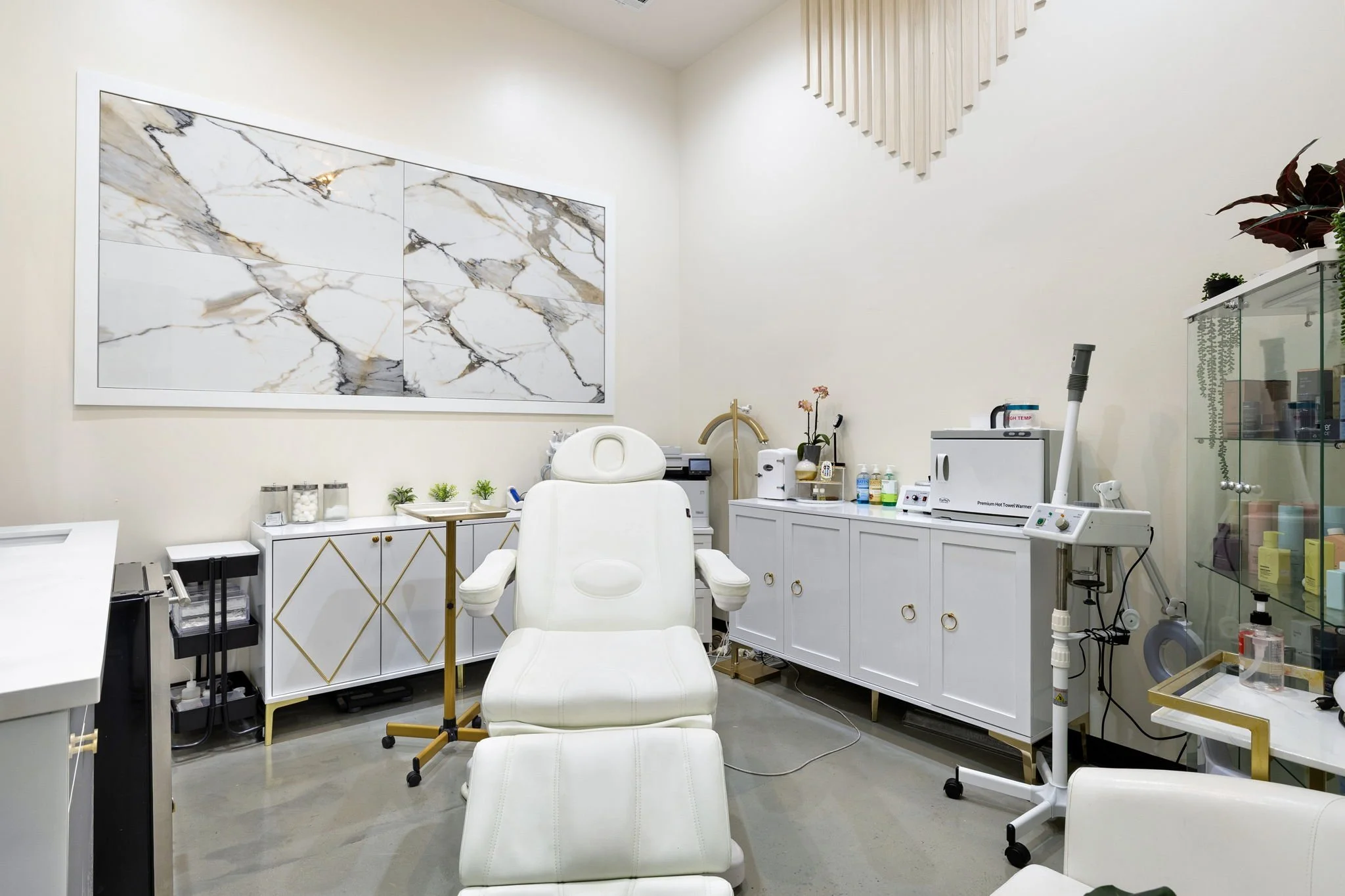 A clean, modern medical or spa treatment room with white leather chair, medical equipment, and marble wall art.