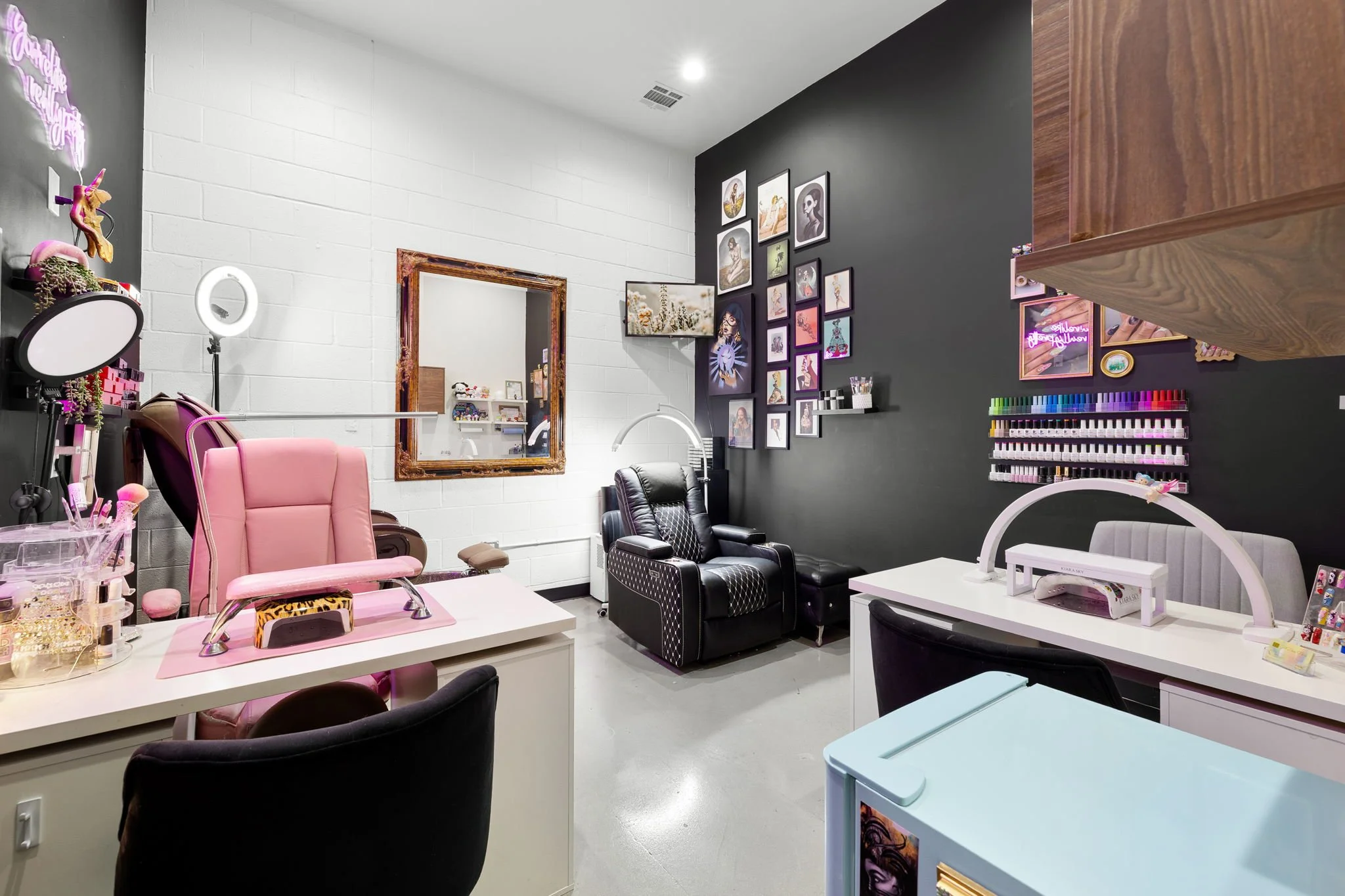 Interior of a nail salon with black and white walls, nail polish display, manicure station, and nail technician chairs.