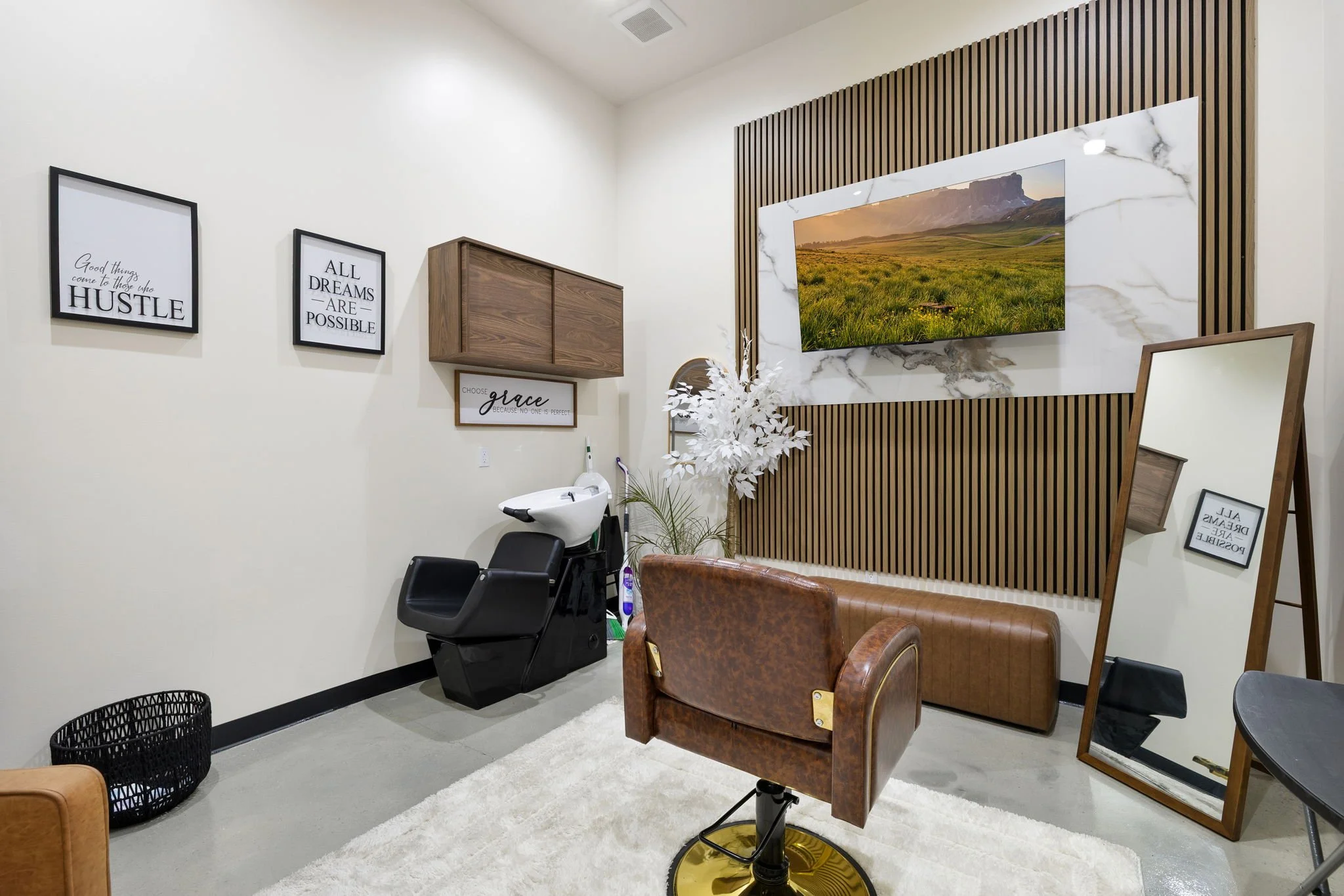 Interior of a salon or beauty studio with a connected chair, mirror, wall art, a TV, a mirror, and decorative plants.