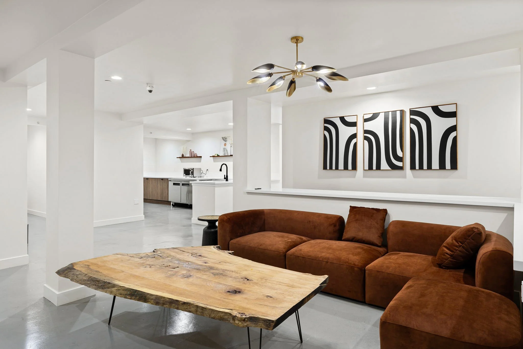 Living room with a brown sofa, a wooden coffee table, and black and white abstract wall art, with a modern ceiling light fixture.