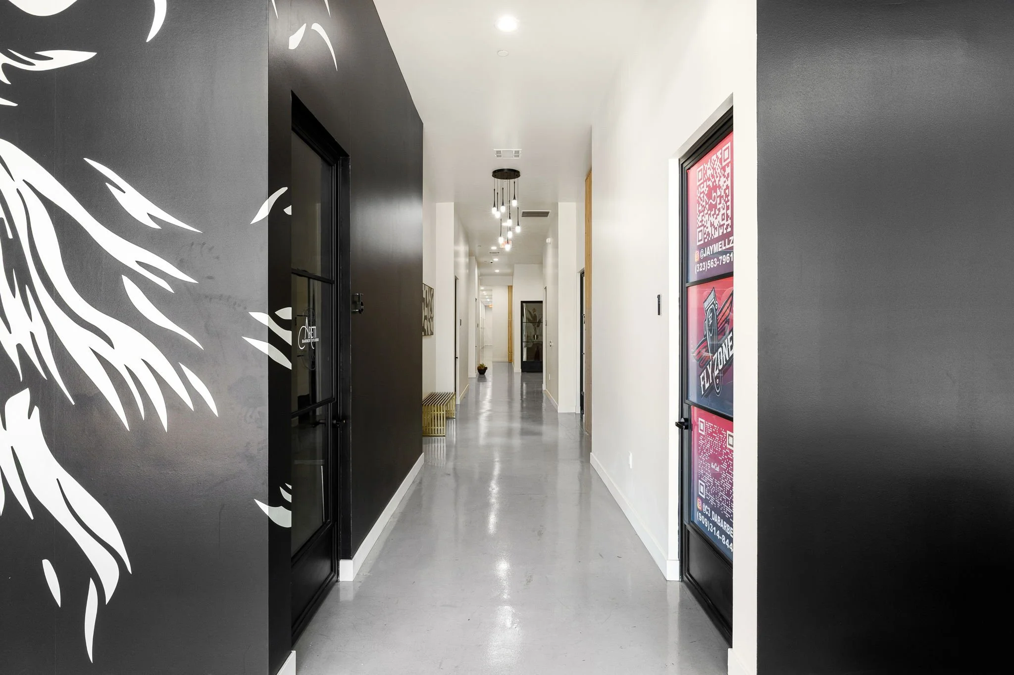 Modern hallway with black and white walls, hanging light fixtures, decorative wall art, and a bench at the end.