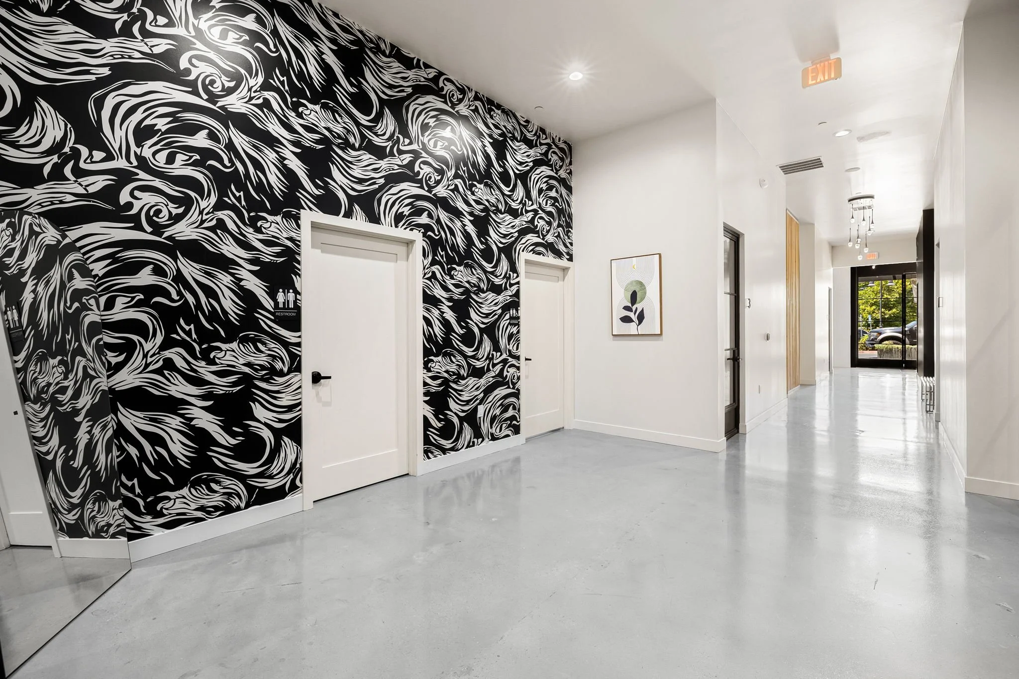Modern interior hallway with white and black swirling wall design, white walls, polished concrete floor, and black-framed glass door at the end.