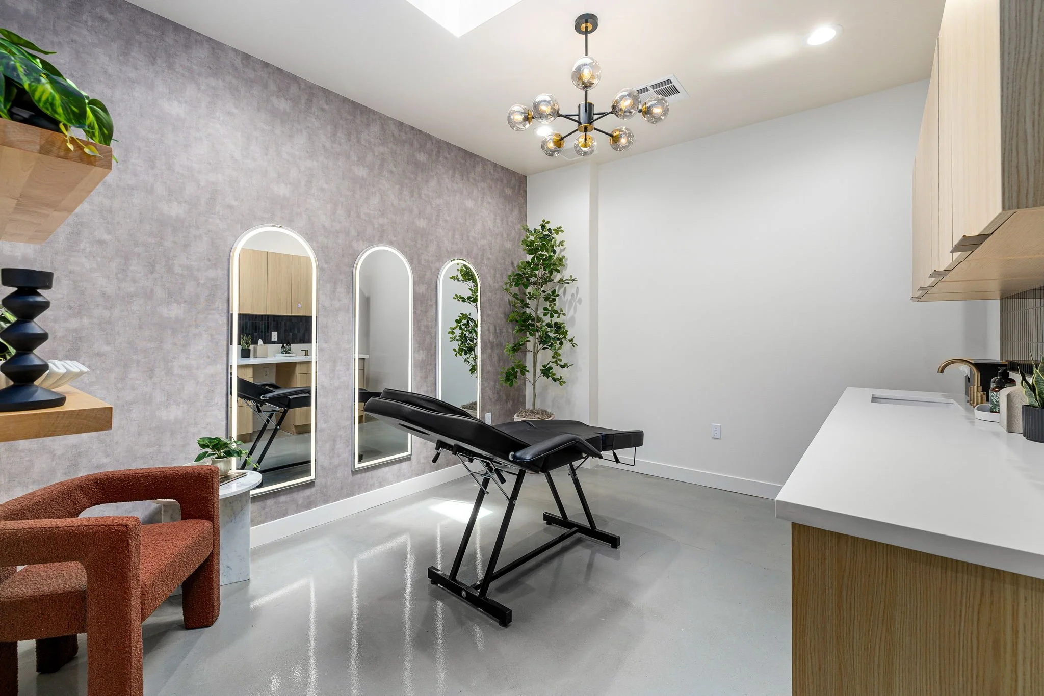 A modern wellness or massage room with a massage table, a single chair, mirrors, and plants.