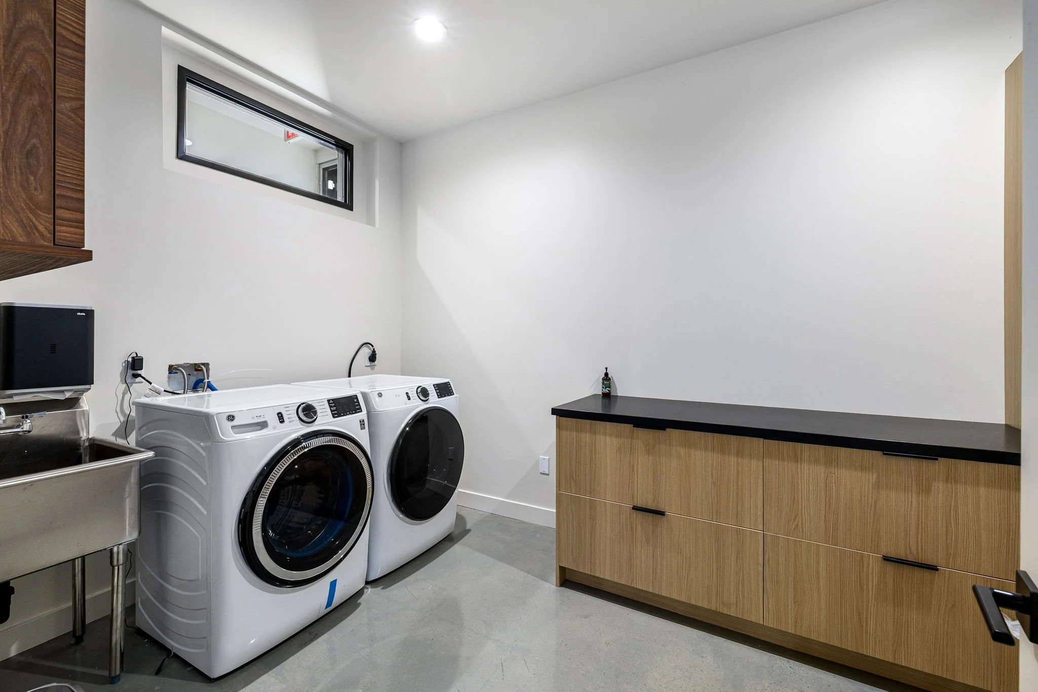 A laundry room with a front-loading washer and dryer, a utility sink, and a wooden cabinet against the wall.