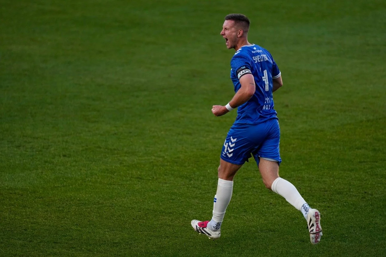 A soccer player wearing a blue uniform with the number 11, celebrating on the field with an excited expression.