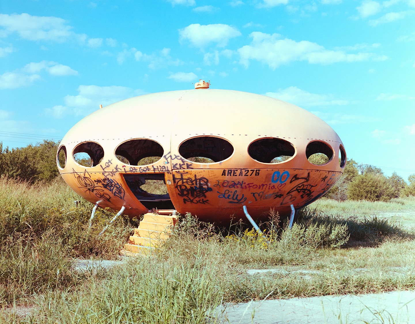 Abandoned orange UFO with graffiti on the outside in a Texas field of grass.