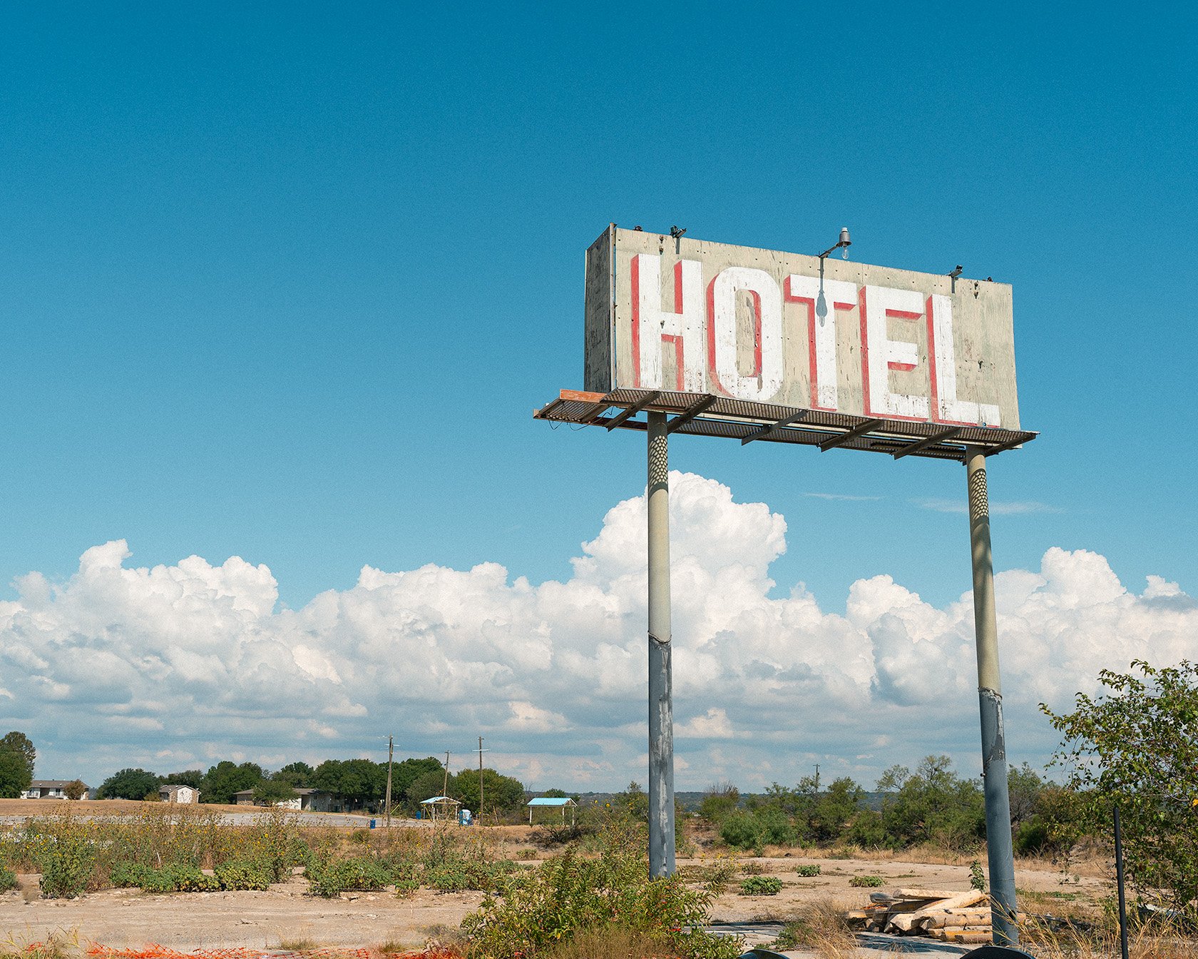 Old abandoned hotel billboard sign in the West Texas landscape, thick white clouds in a vibrant blue sky, Fine art photography, Western art.