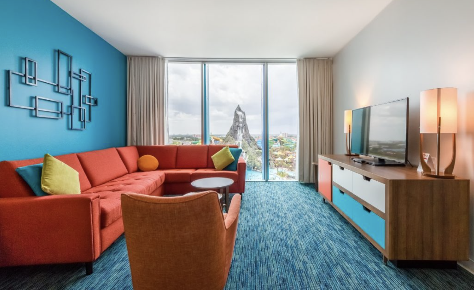 Living room with a red sectional sofa, colorful pillows, and a view of a mountain and theme park outside large windows.