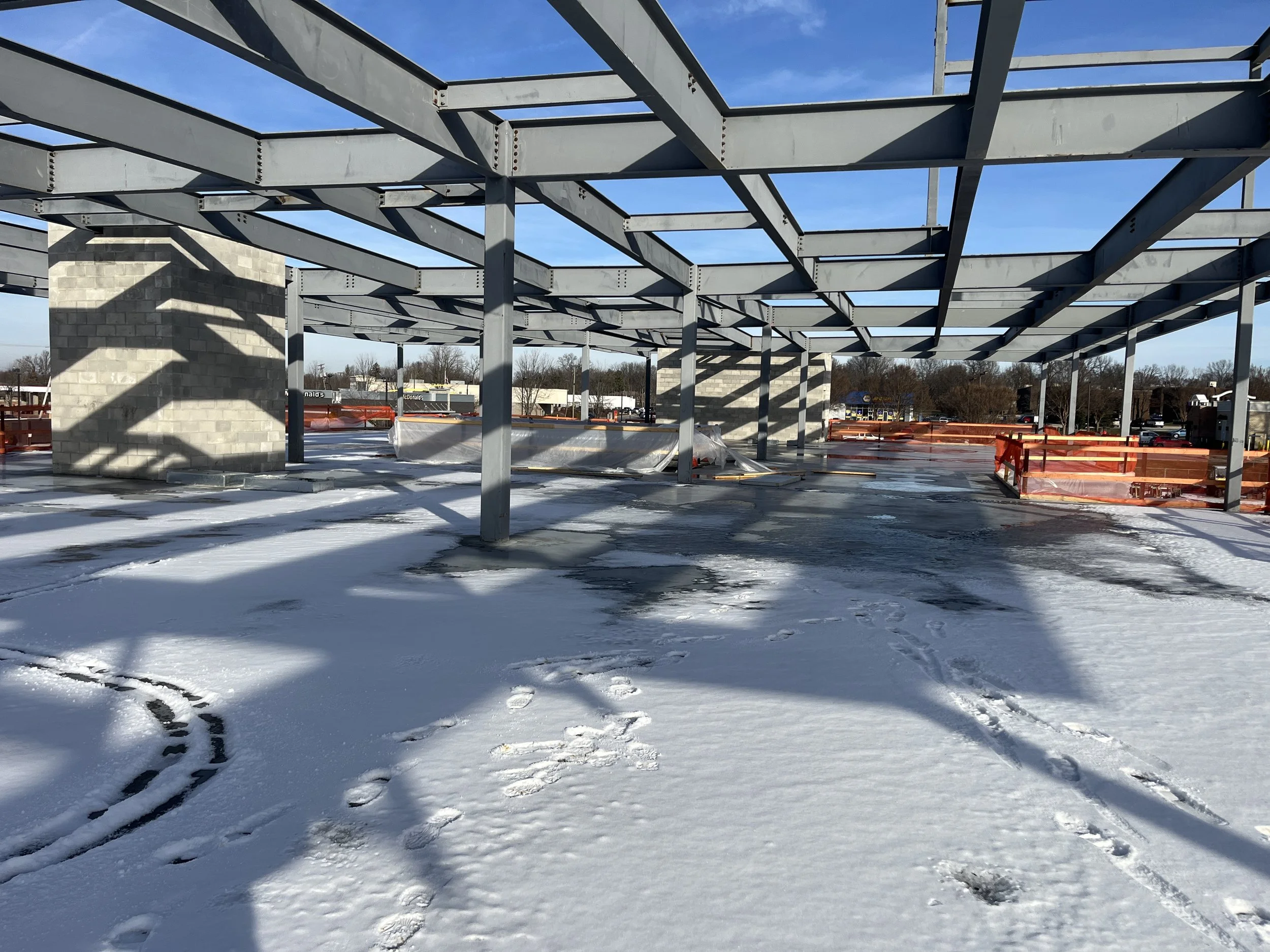 Snow-covered construction site with steel framing and concrete block structures under clear blue sky.
