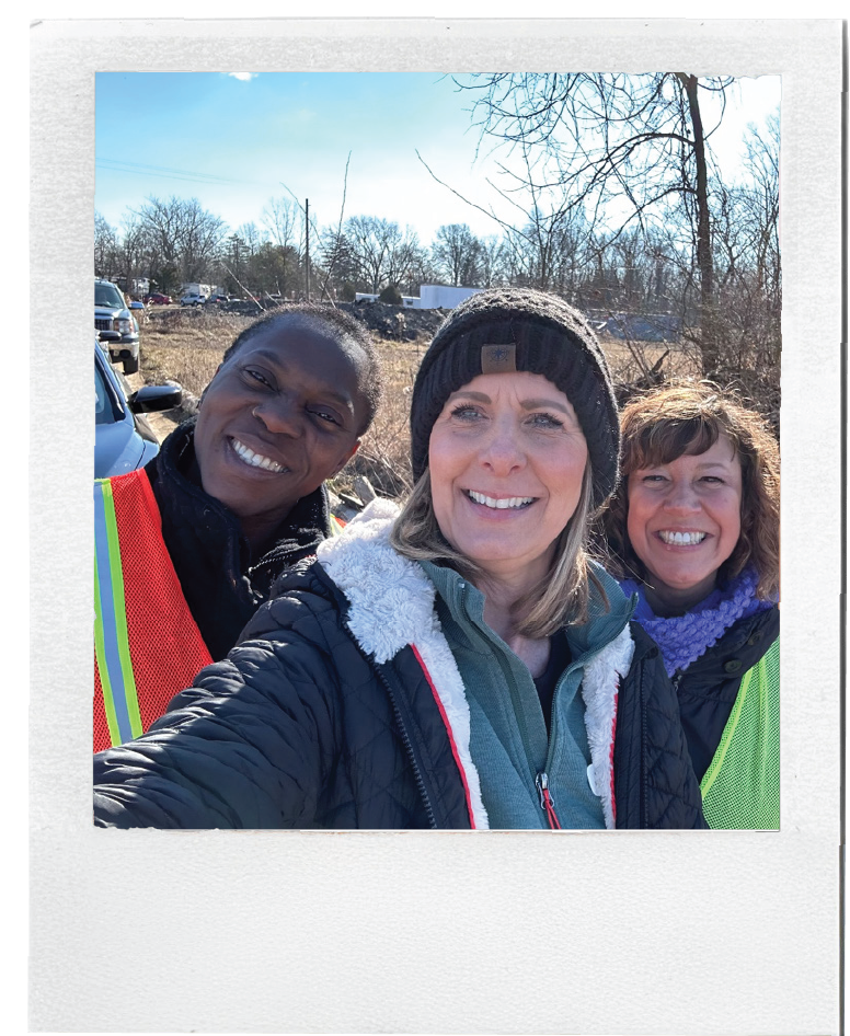 Polaroid-style photo of three volunteers posing outdoors during a community service project.