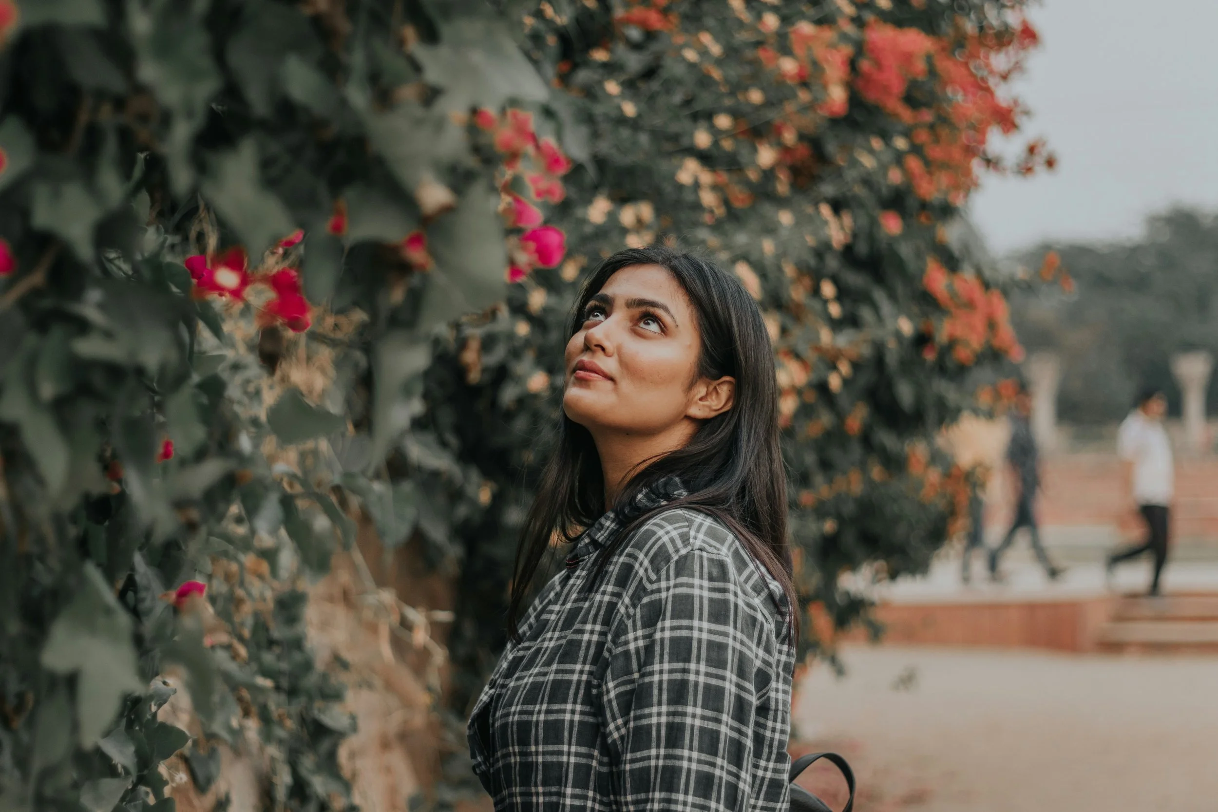 South Asian woman looking up at flowering vines along a garden wall.