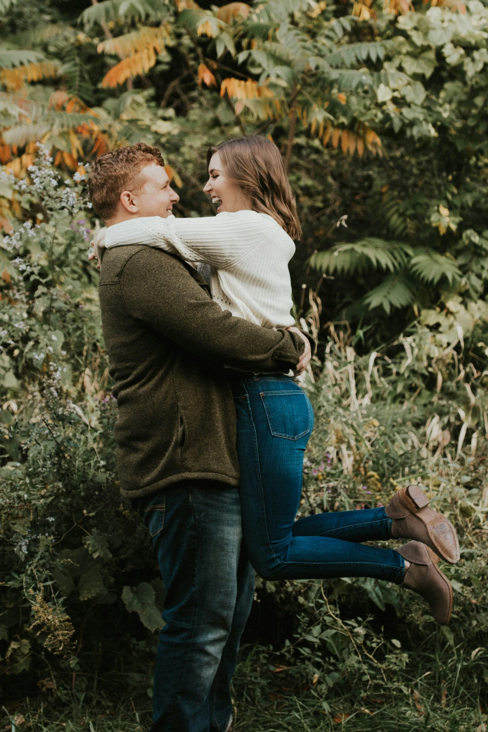 Couple smiling while hugging mid-air in front of greenery.