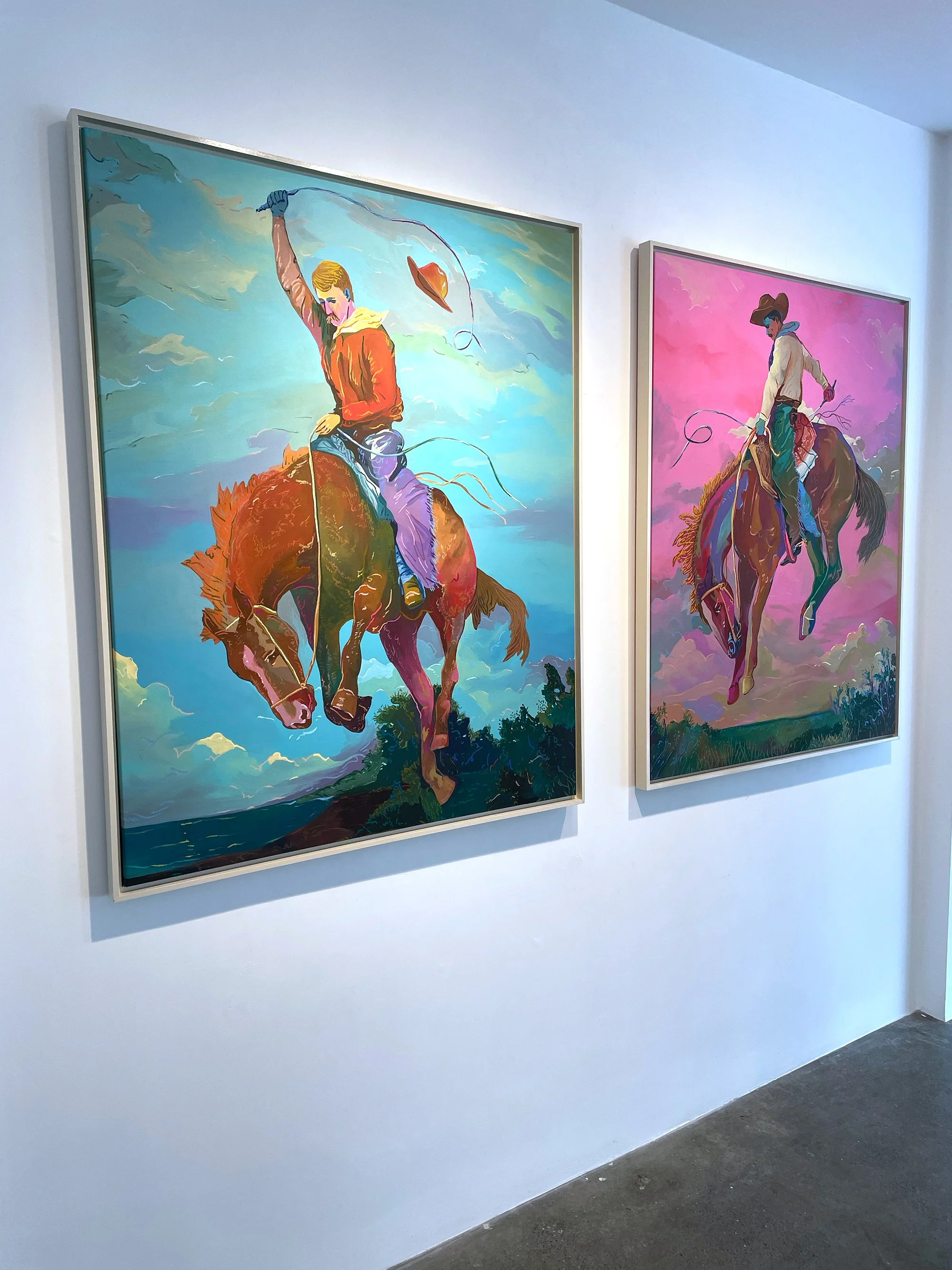 Two colorful paintings of cowboys riding horses, hanging on a gallery wall.
