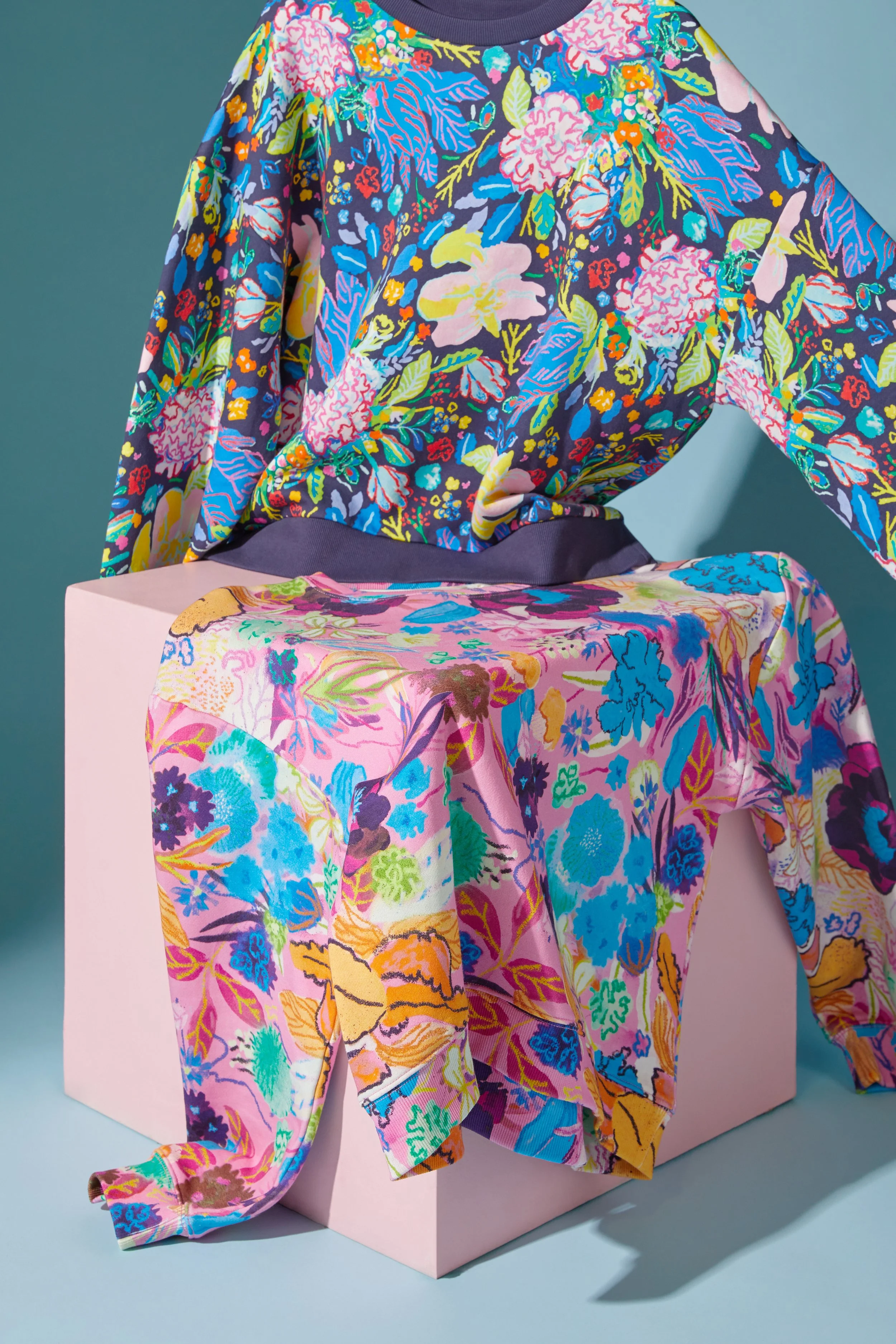 Colorful floral patterned clothing displayed on a white platform with a muted teal background.