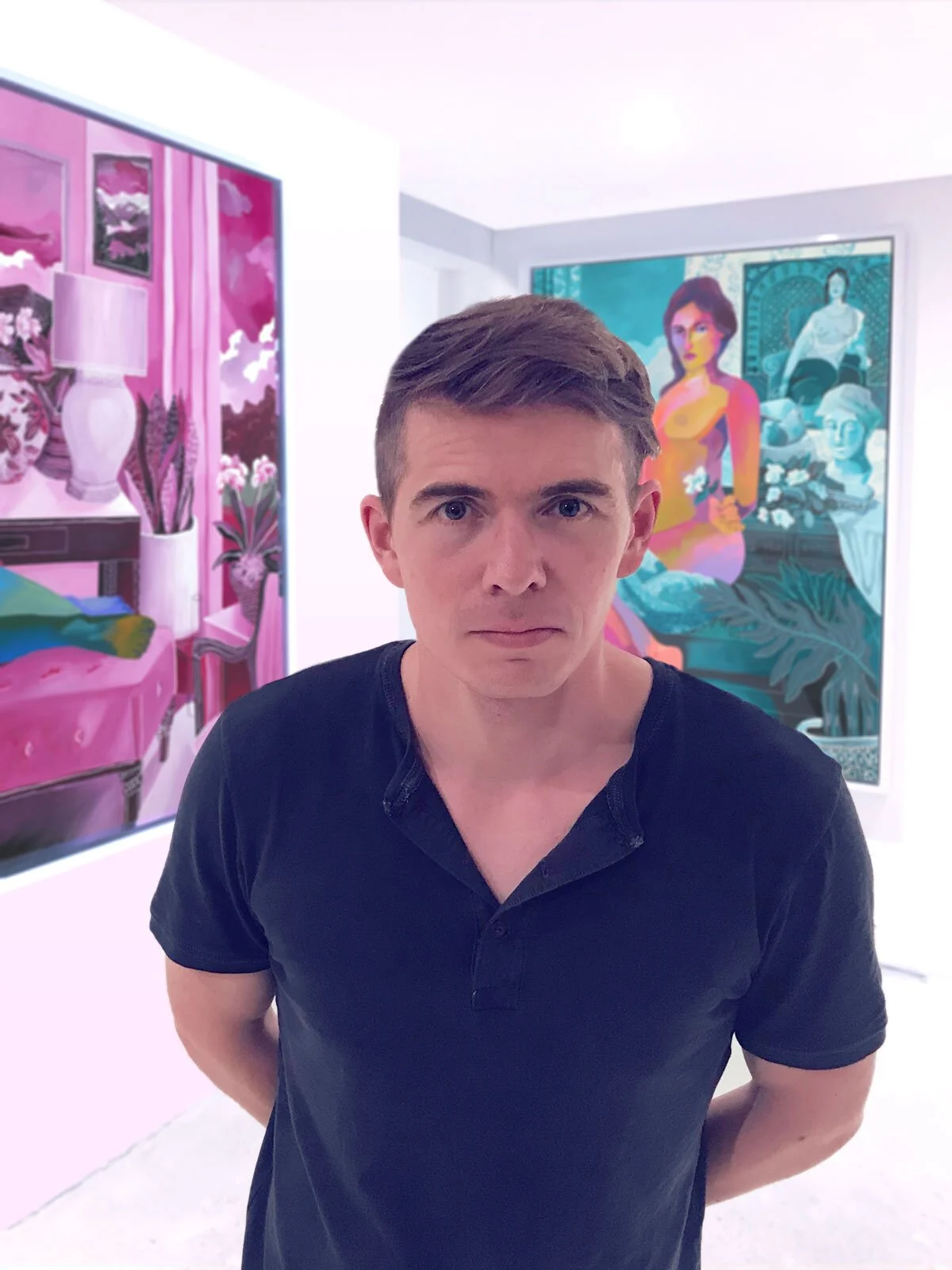 A young man with brown hair, wearing a black shirt, stands in an art gallery with colorful paintings on the walls behind him.