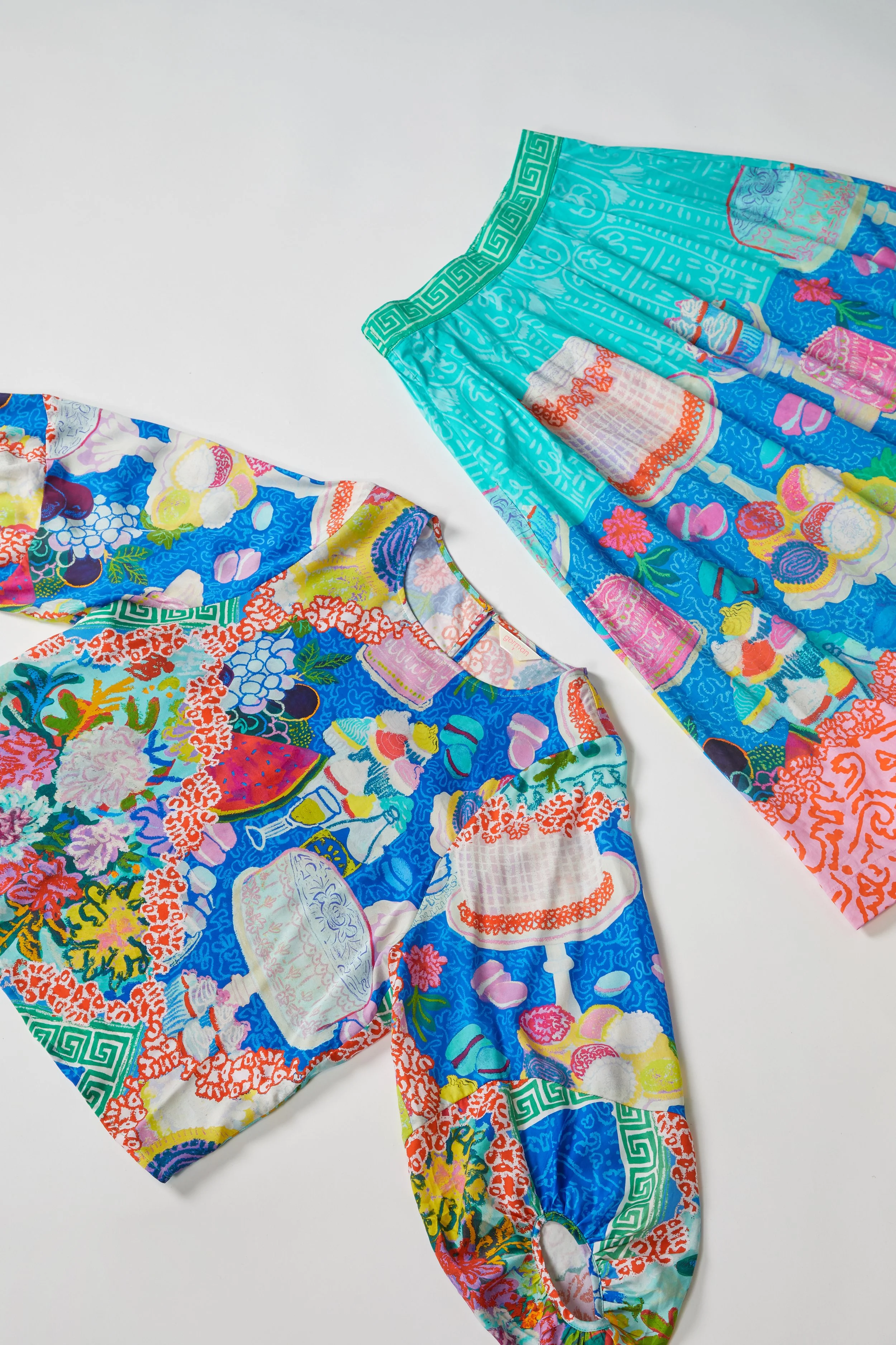 Colorful, patterned pajama top and pants with images of cakes, desserts, and floral designs, laid out on a white background.