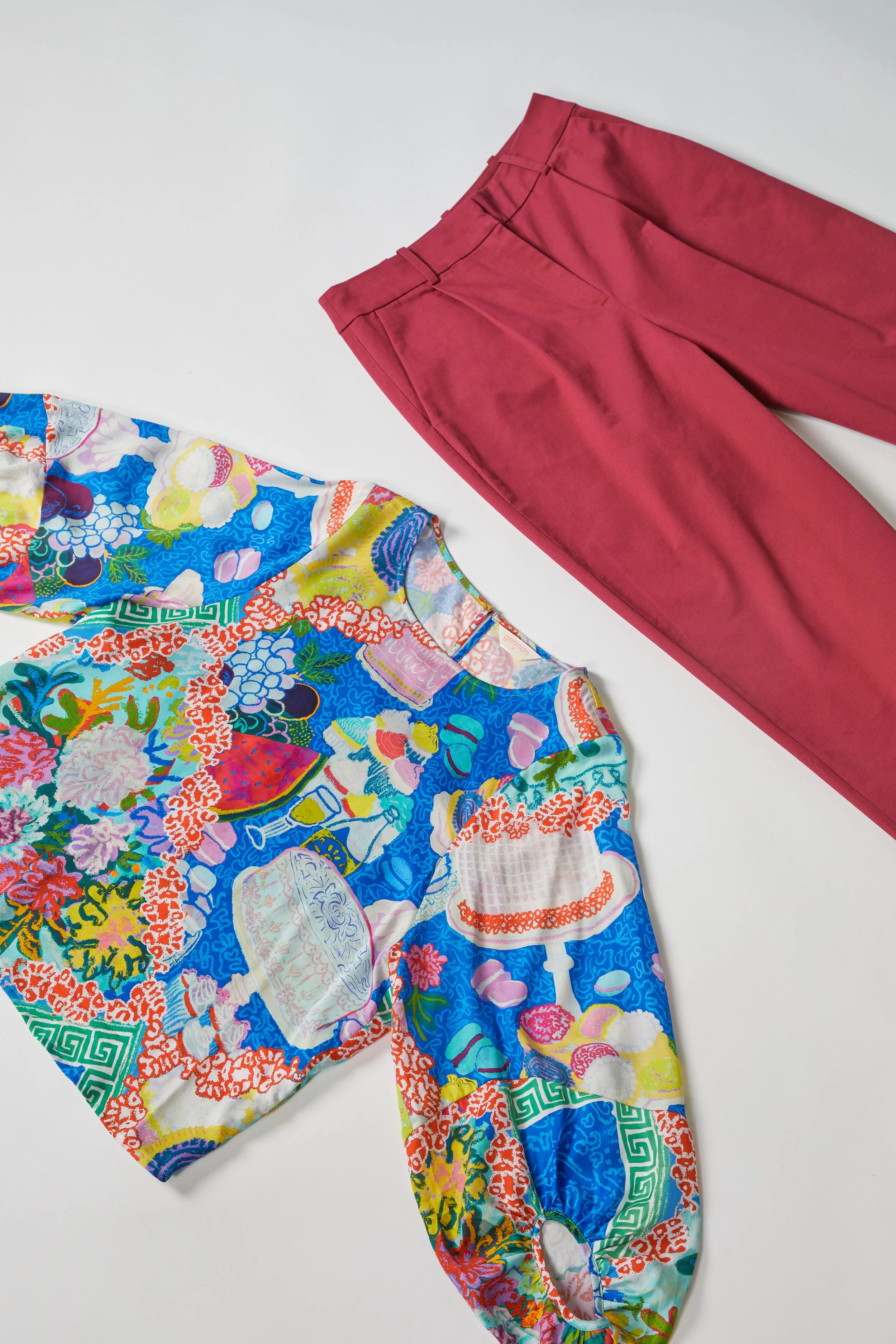 Pair of red trousers and a colorful embroidered top laid out on a white surface.