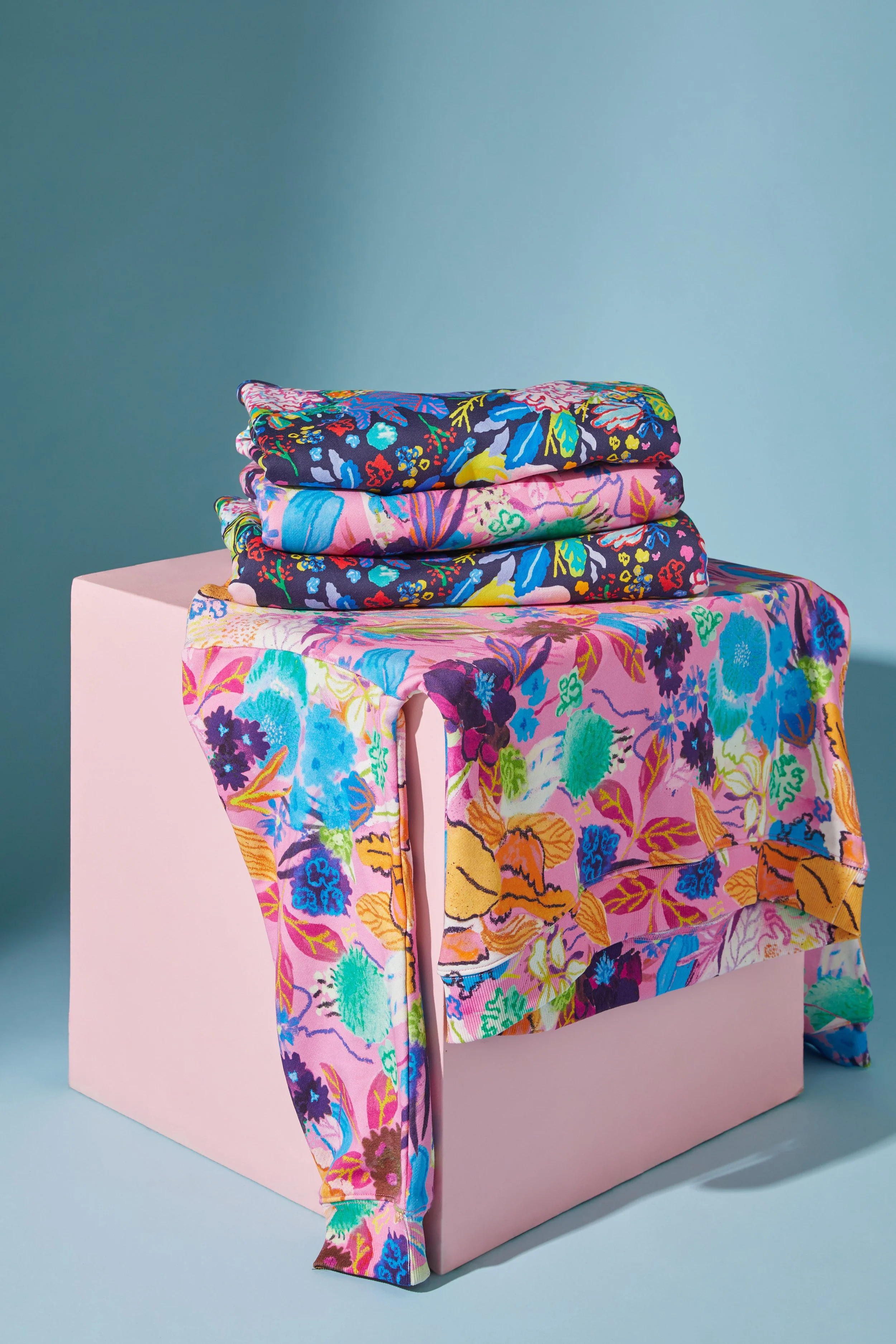 A stack of folded, colorful floral-printed fabric resting on a pink box, with a matching floral fabric draping over the edge.