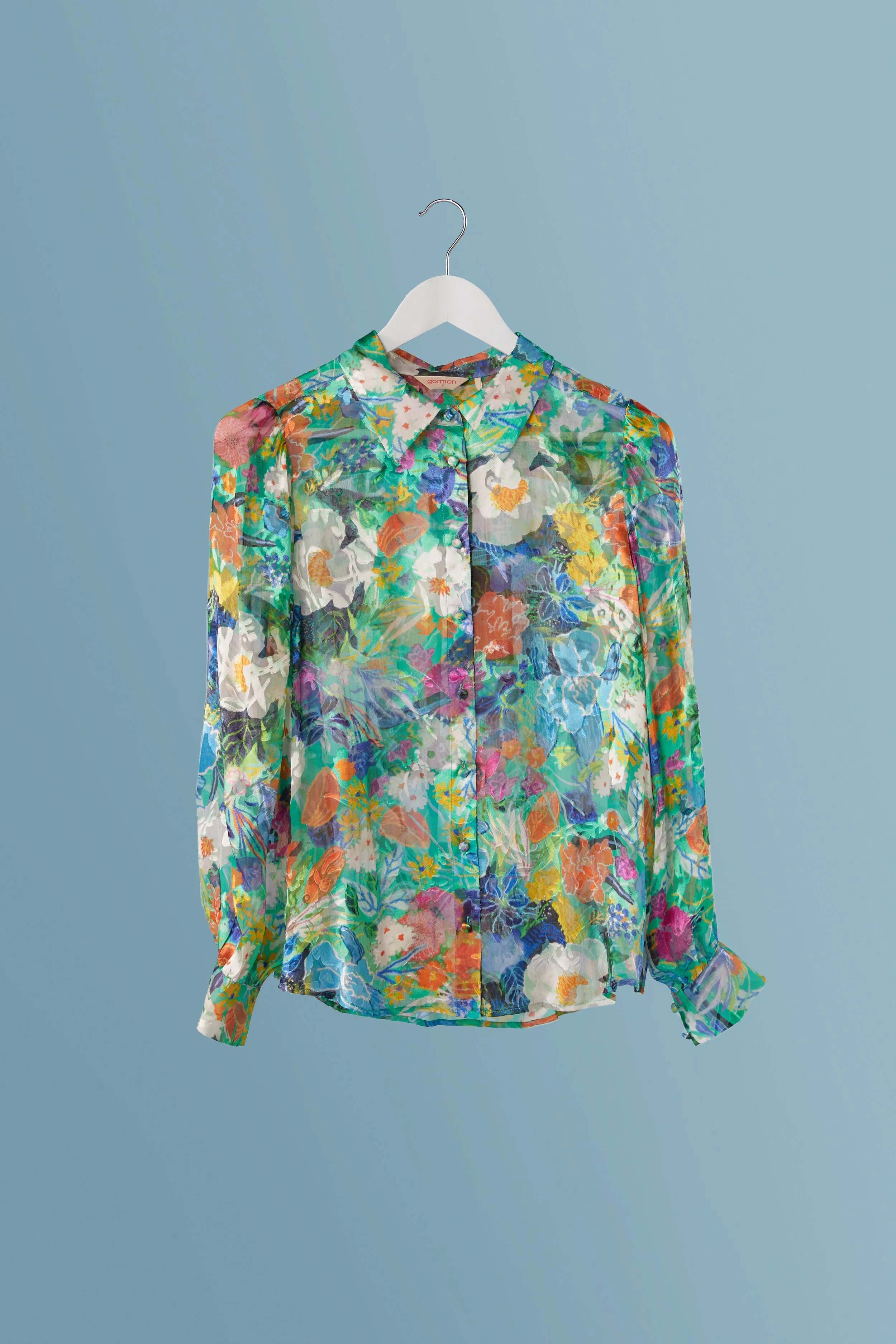 Colorful floral patterned blouse hanging on a white hanger against a light blue background.