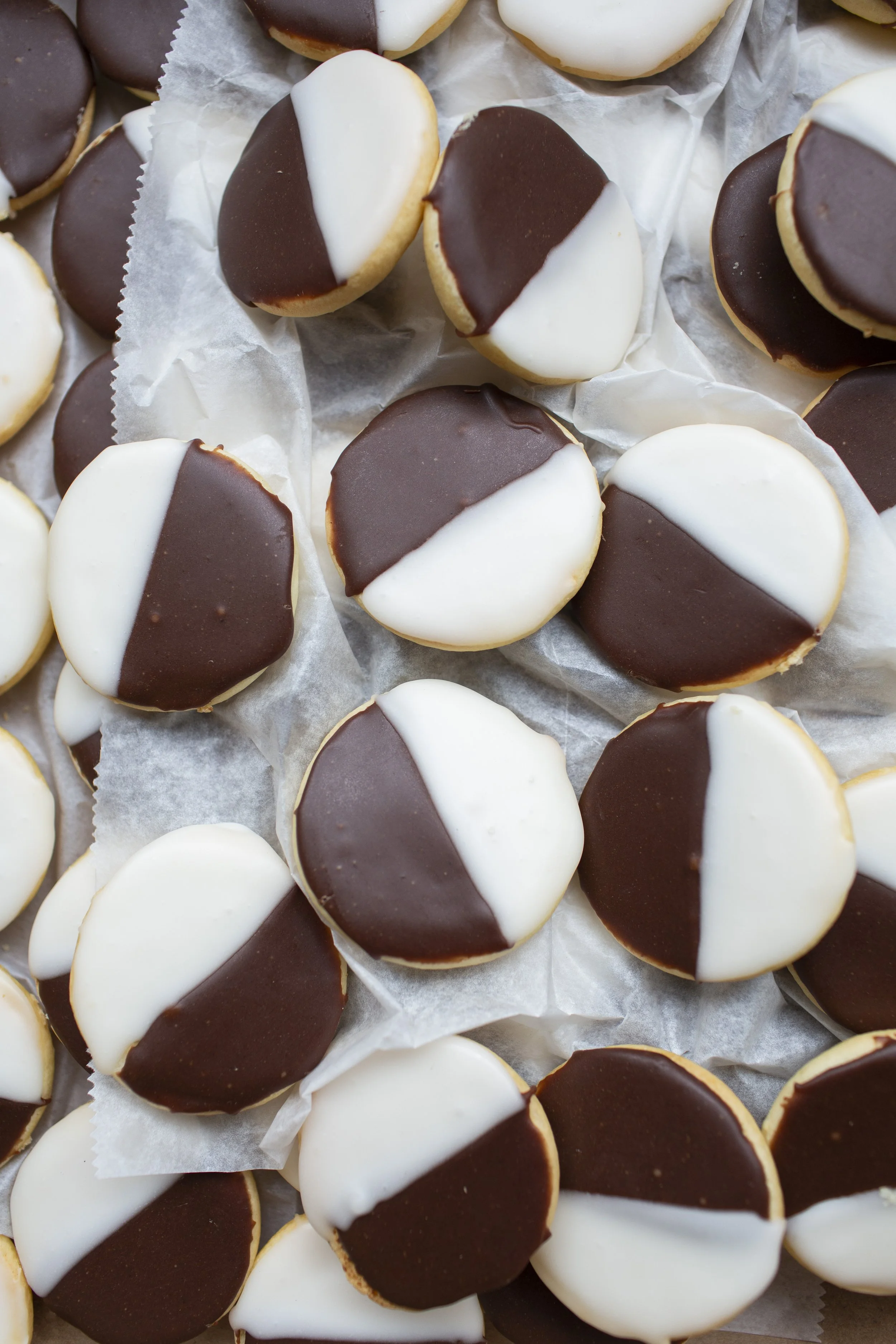 Assortment of freshly baked Black & White cookies on wax paper, stacked on other Black & White cookies.