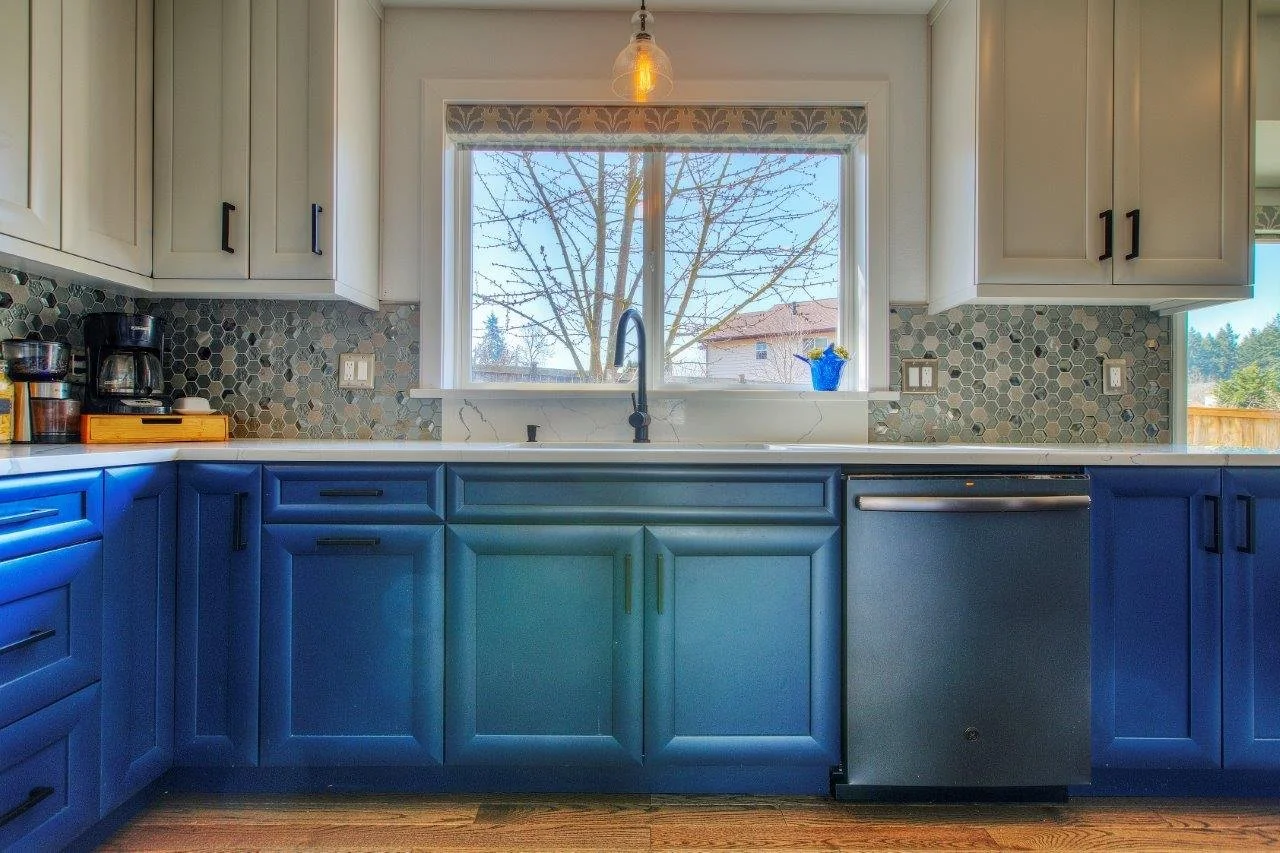 Kitchen sink centered under a large window with custom blue cabinetry in a University Place home renovation.