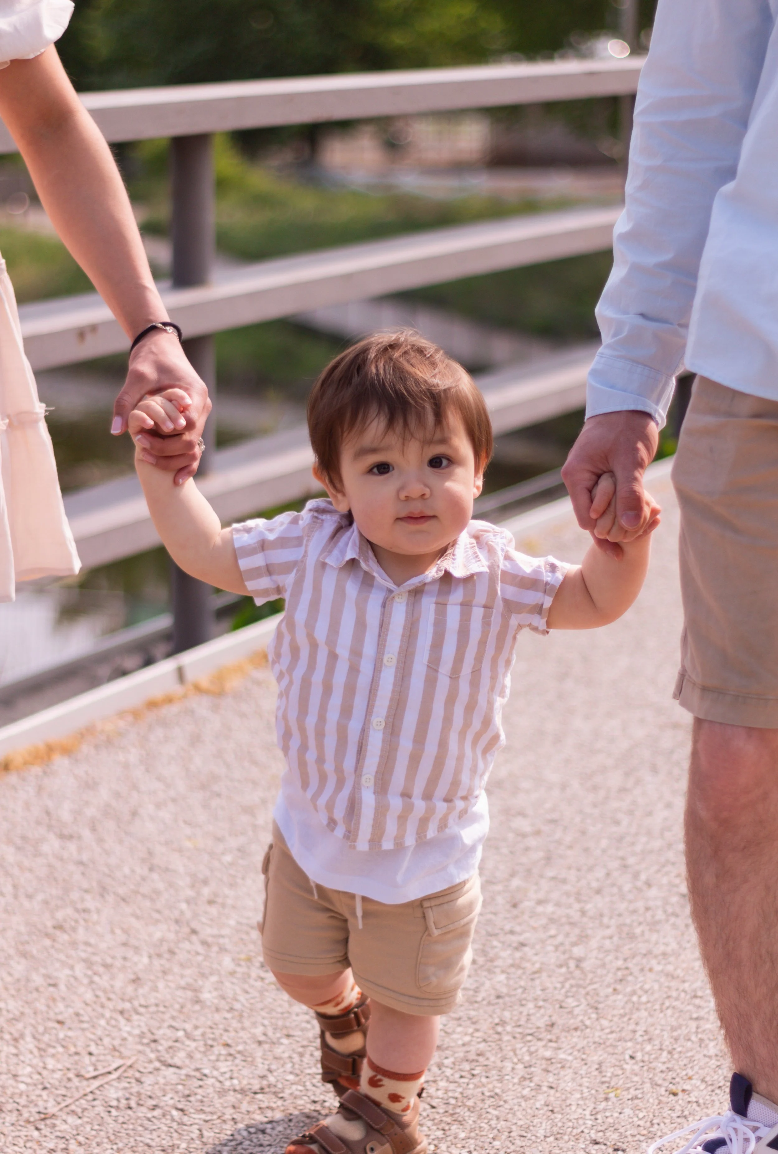 Young boy holding hands with two adults, walking outdoors on a sunny day