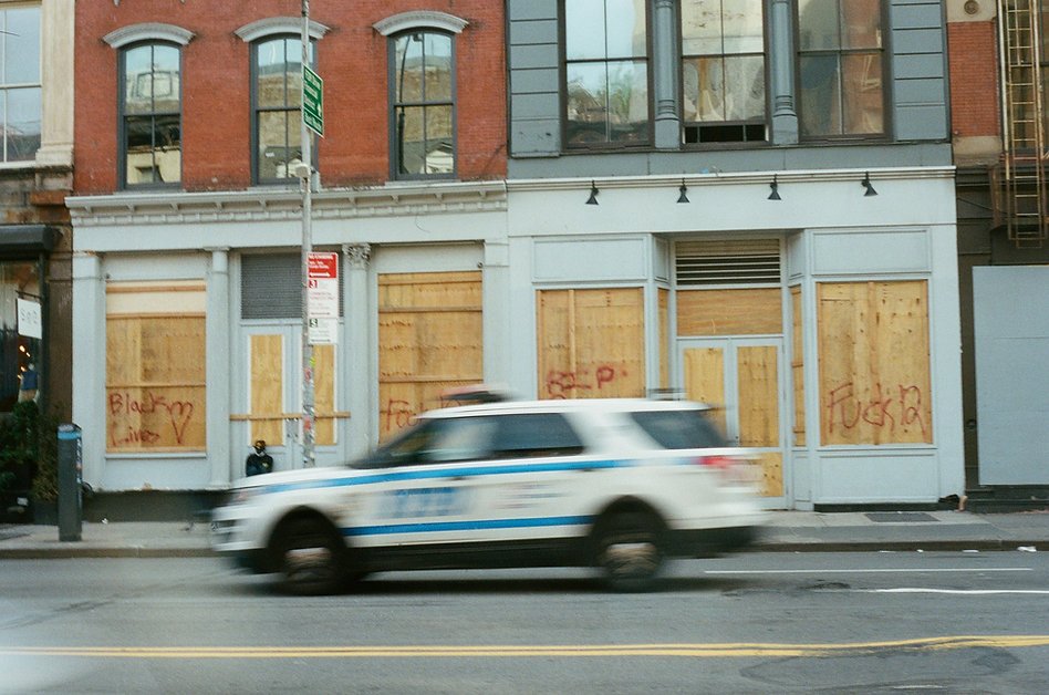 35mm photo of moving police SUV in front of a boarded up retail store in SoHo New York City. Photo by Brianna Mancini