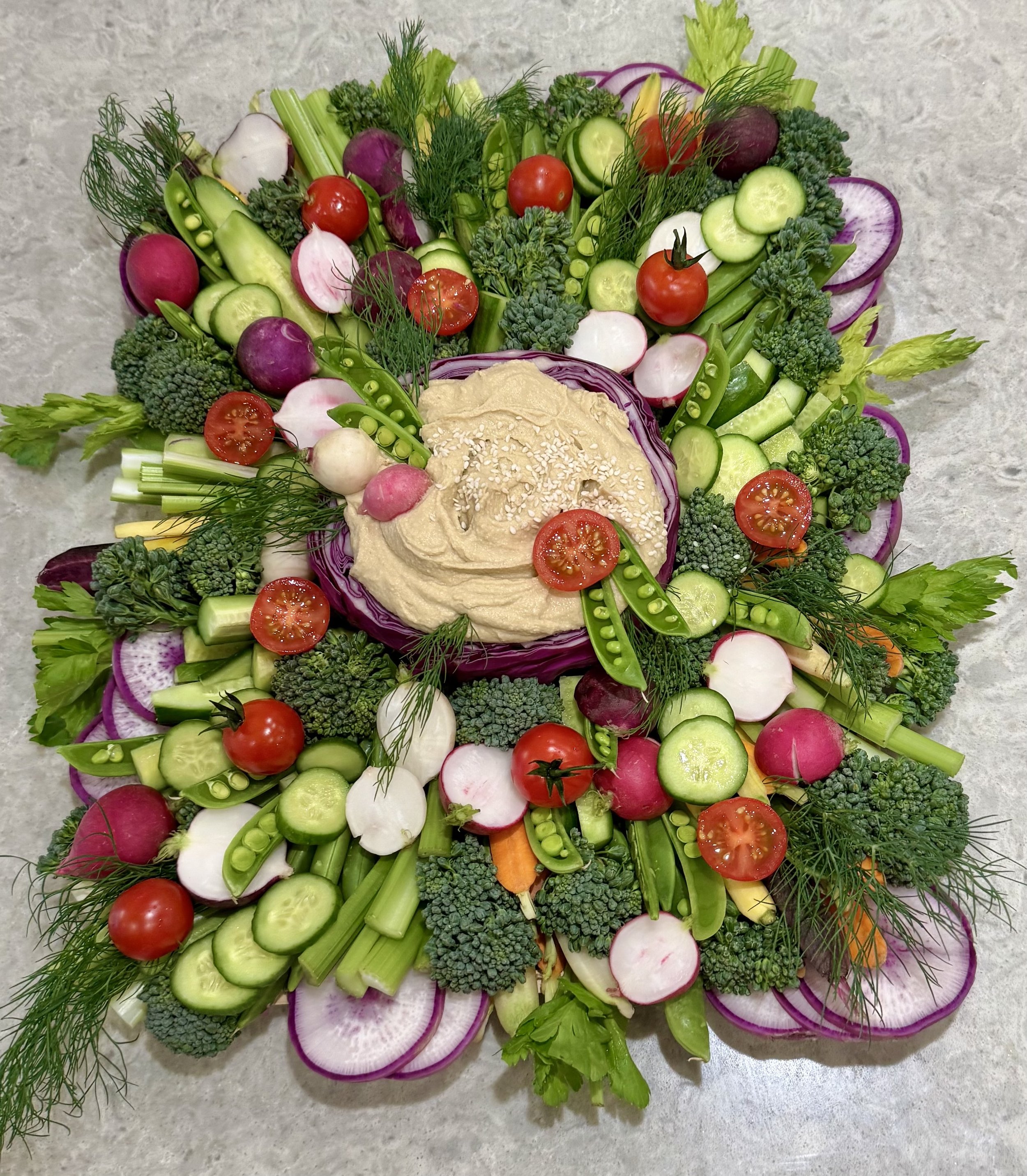 Vegetable platter with cherry tomatoes, cucumber slices, radishes, celery, broccoli, green peas, sprouts, herbs, and a central dip.