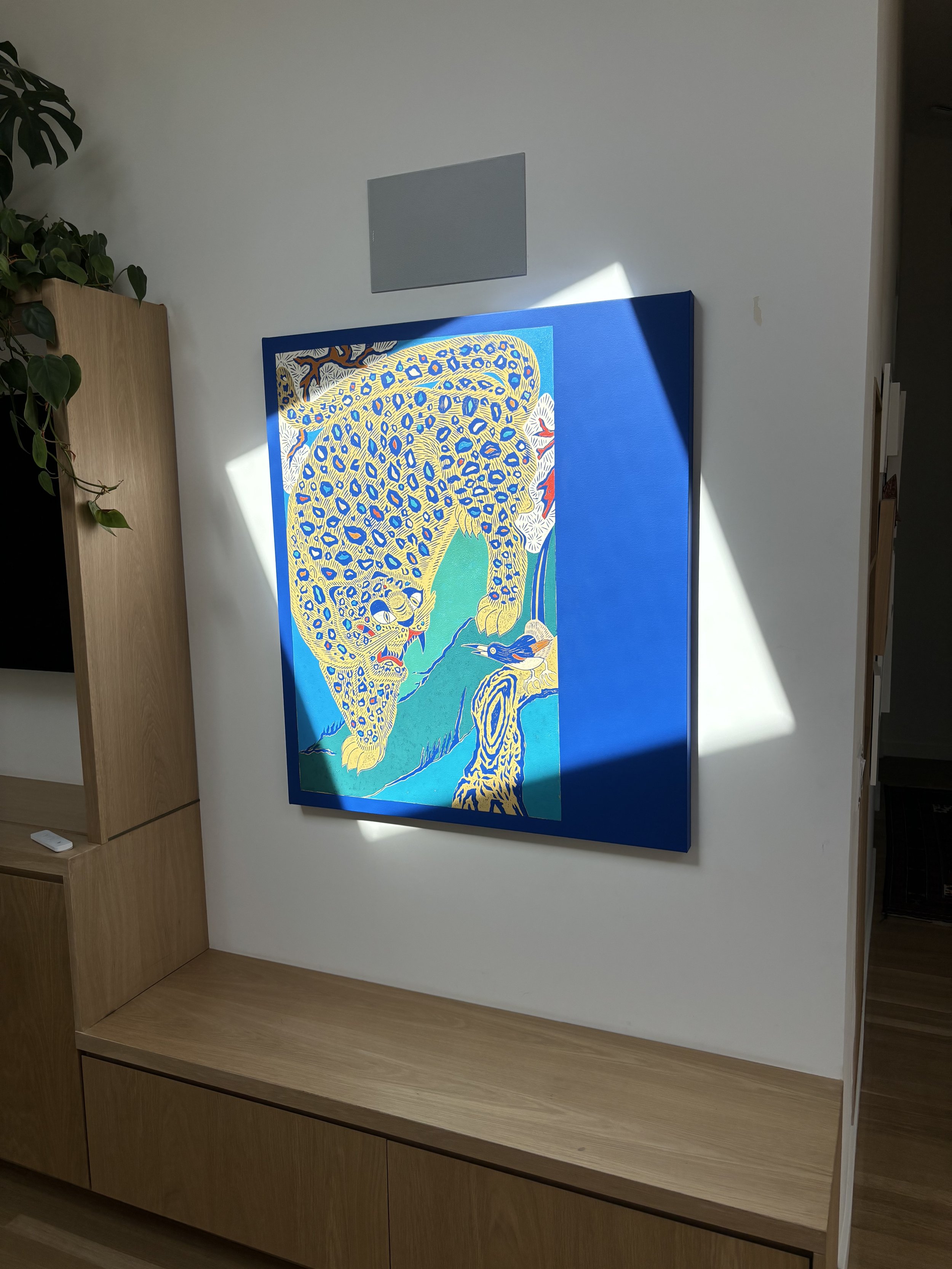 Colorful artwork of a jaguar on a vibrant blue background hanging on a white wall in a modern room.