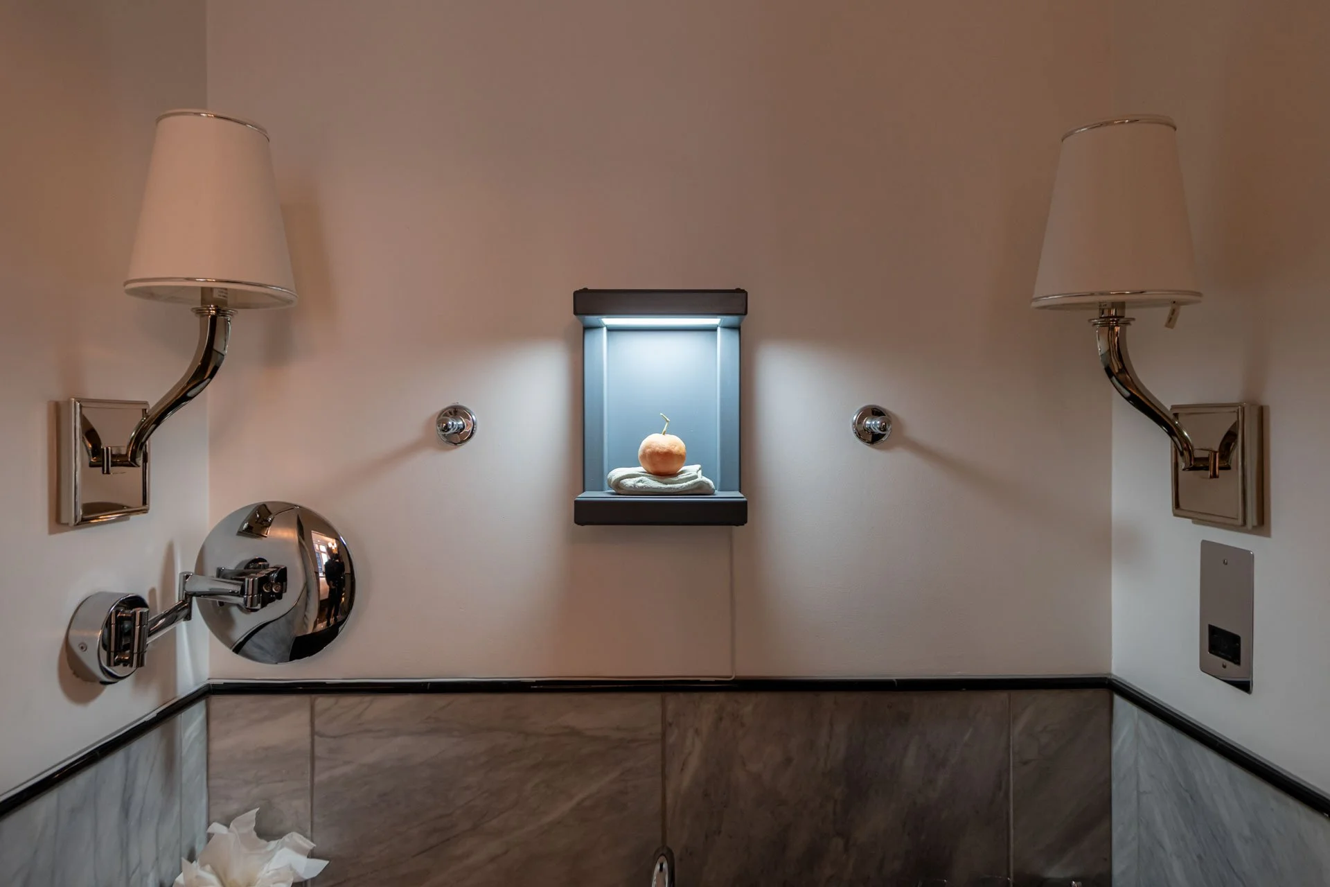 Bathroom installation view with a small lit display niche between two wall   lamps, turning an everyday space into a micro-gallery