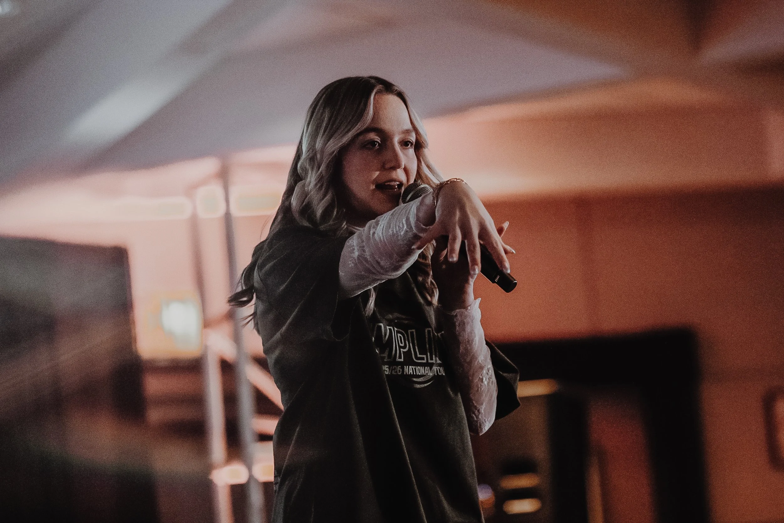 A woman demonstrating dance or fitness moves in front of a group of children in a dance studio with dim lighting.
