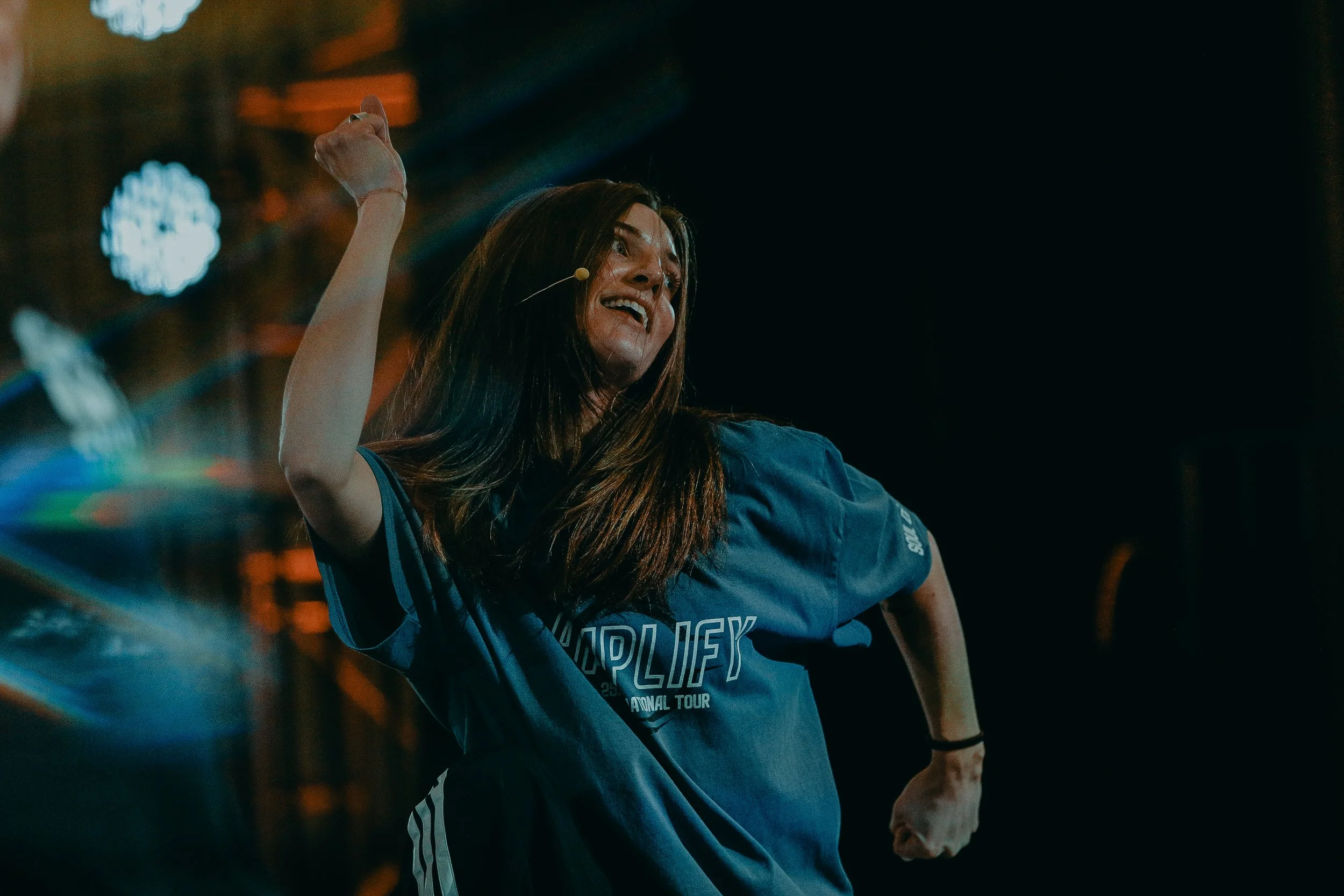 A dance instructor leading a class in a dimly lit studio with students following in the background.