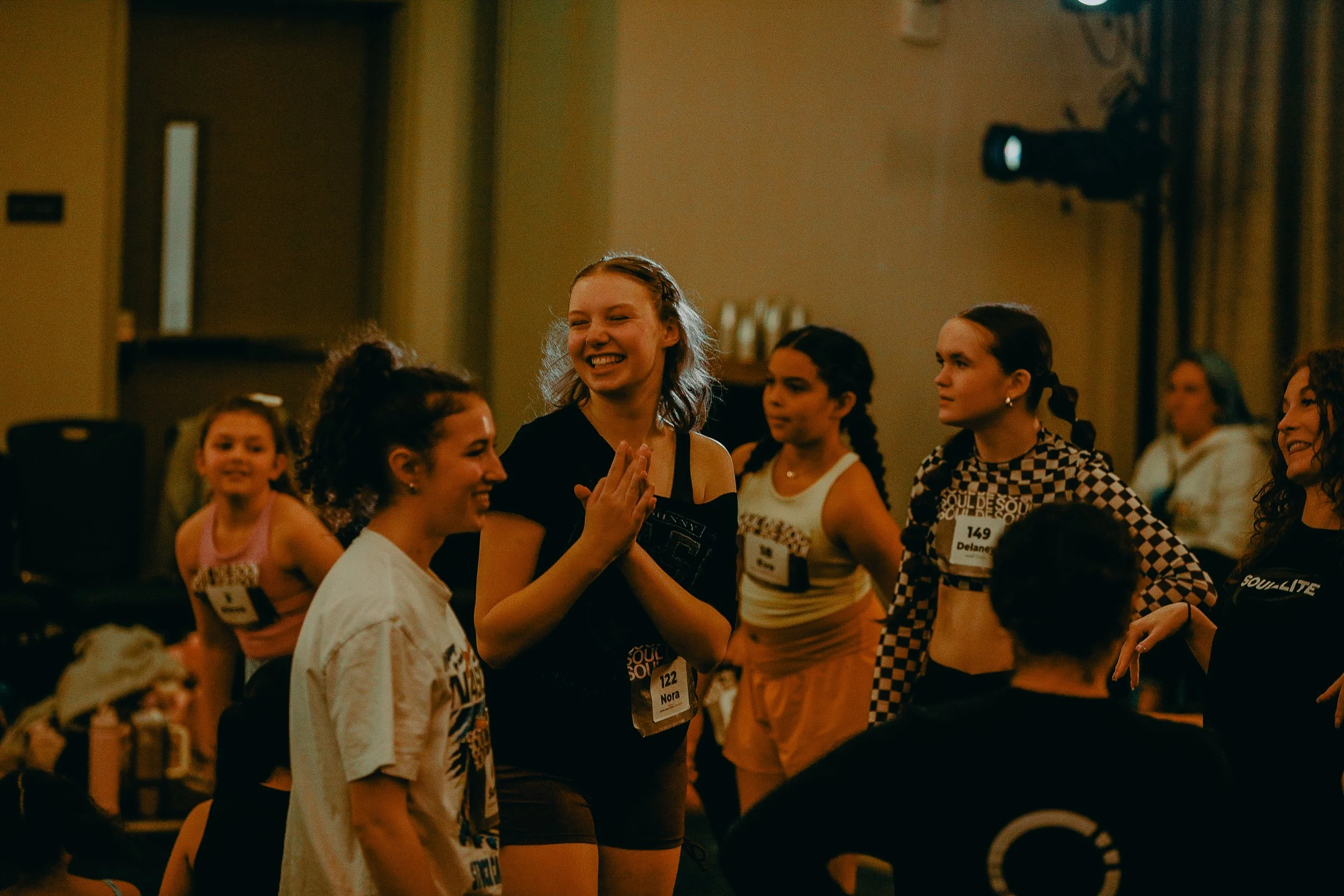 Group of women and girls at an indoor event, some with name tags, engaging in conversation and smiling.
