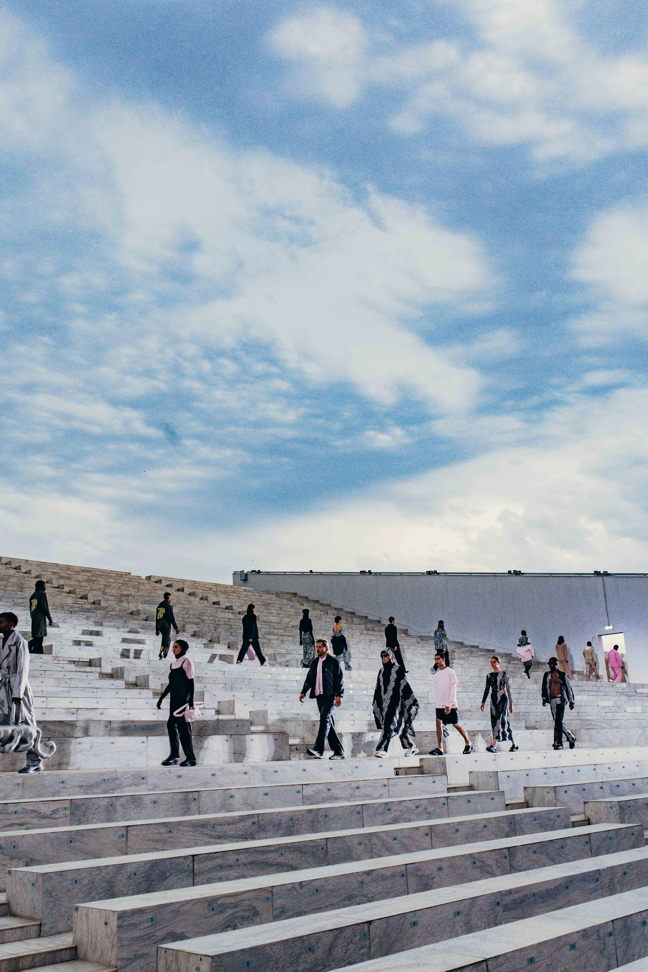 People walking on large, tiered marble steps outdoors under a partly cloudy sky.