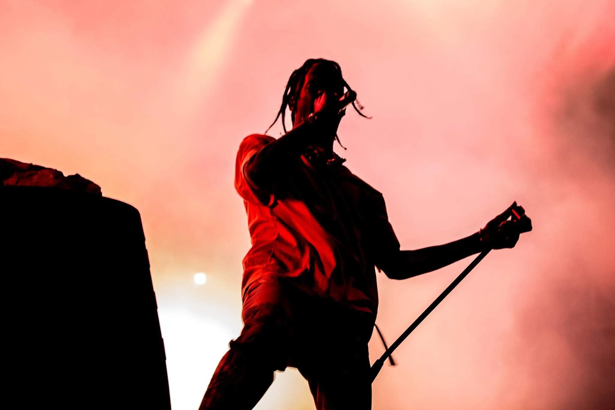 Silhouette of a performer on stage with a microphone, illuminated by reddish-orange lighting.