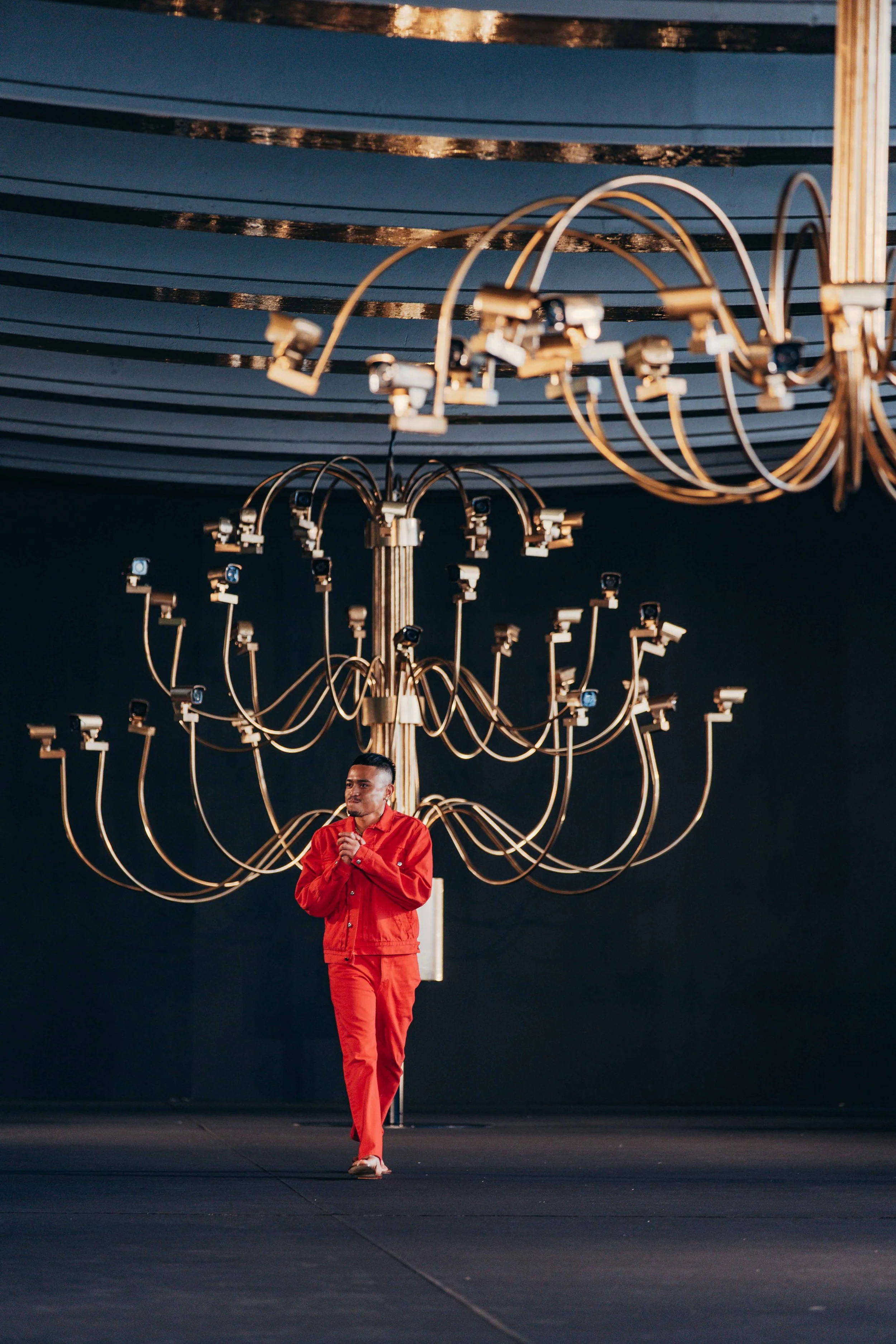 A man in a red outfit walks on stage under a large ornate chandelier.