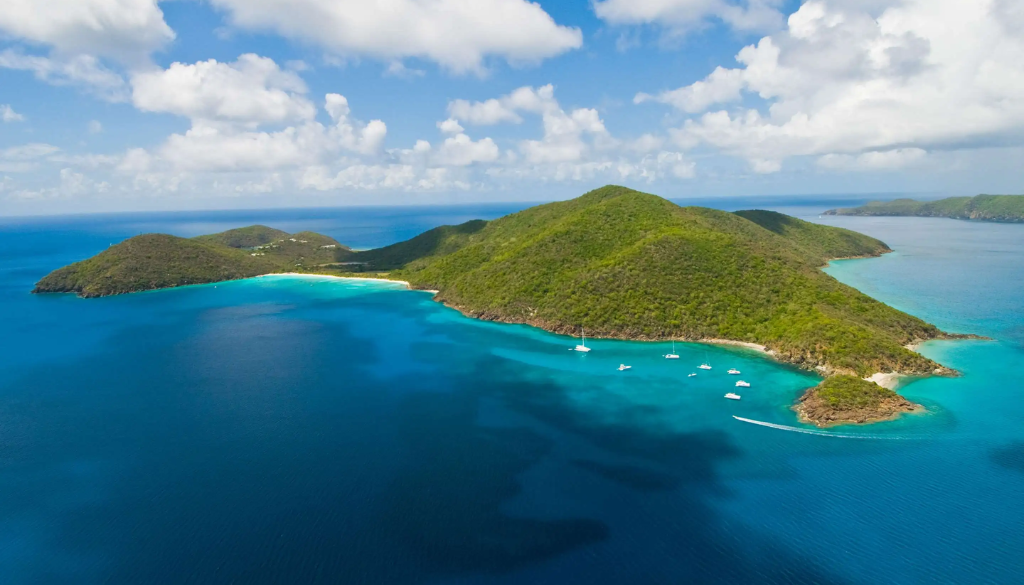 Aerial view of Guana Island private resort in the British Virgin Islands with lush tropical hillside, crescent beach, and turquoise Caribbean waters