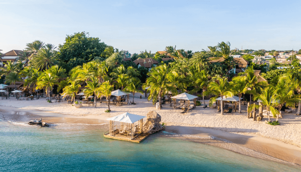 Pristine white sand beach at Baoase Luxury Resort Curaçao with palm trees, calm Caribbean waters, and lush tropical gardens