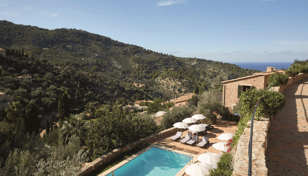 Stone manor facade of La Residencia A Belmond Hotel Mallorca nestled among olive groves in the village of Deià with Tramuntana mountains behind