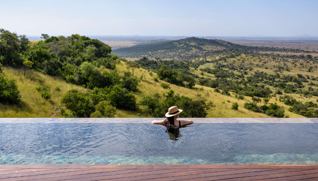 Guest relaxing in an infinity pool at Singita Sasakwa Lodge with panoramic views over the Serengeti plains Tanzania