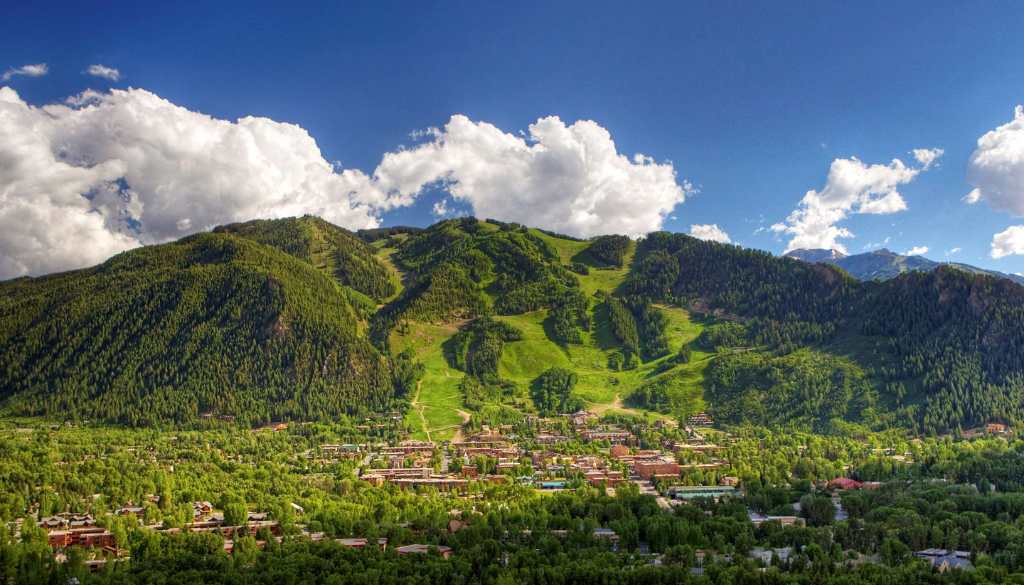 Wide landscape of Aspen Colorado valley surrounded by lush green summer mountains under a bright blue sky