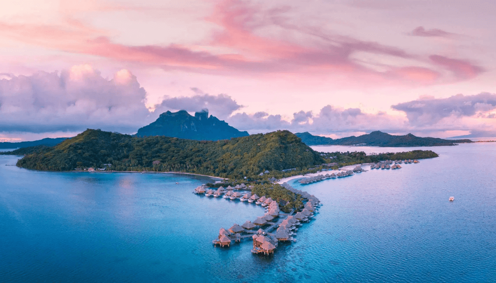 Aerial view of Conrad Bora Bora Nui resort with overwater villas extending over the turquoise lagoon and Mount Otemanu in the background — October honeymoon