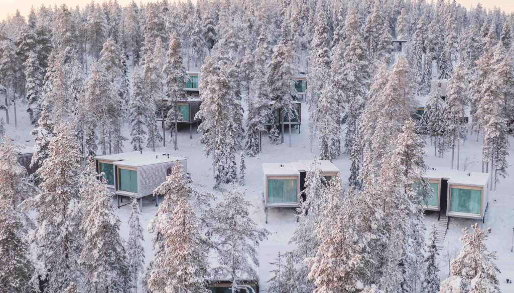 Cozy luxury Arctic treehouse cabin in Finnish Lapland covered in snow with Northern Lights visible in the night sky above the frozen wilderness