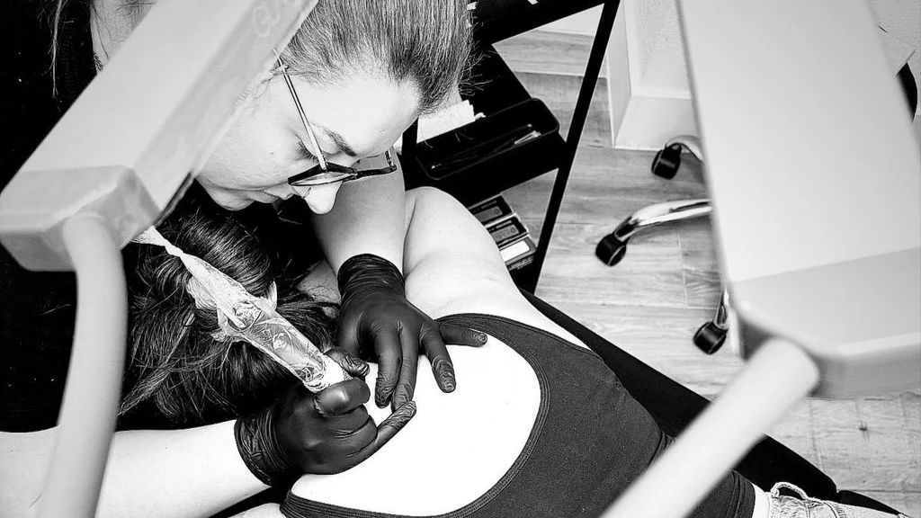 Tattoo artist applying ink to a person's forearm in a tattoo studio.