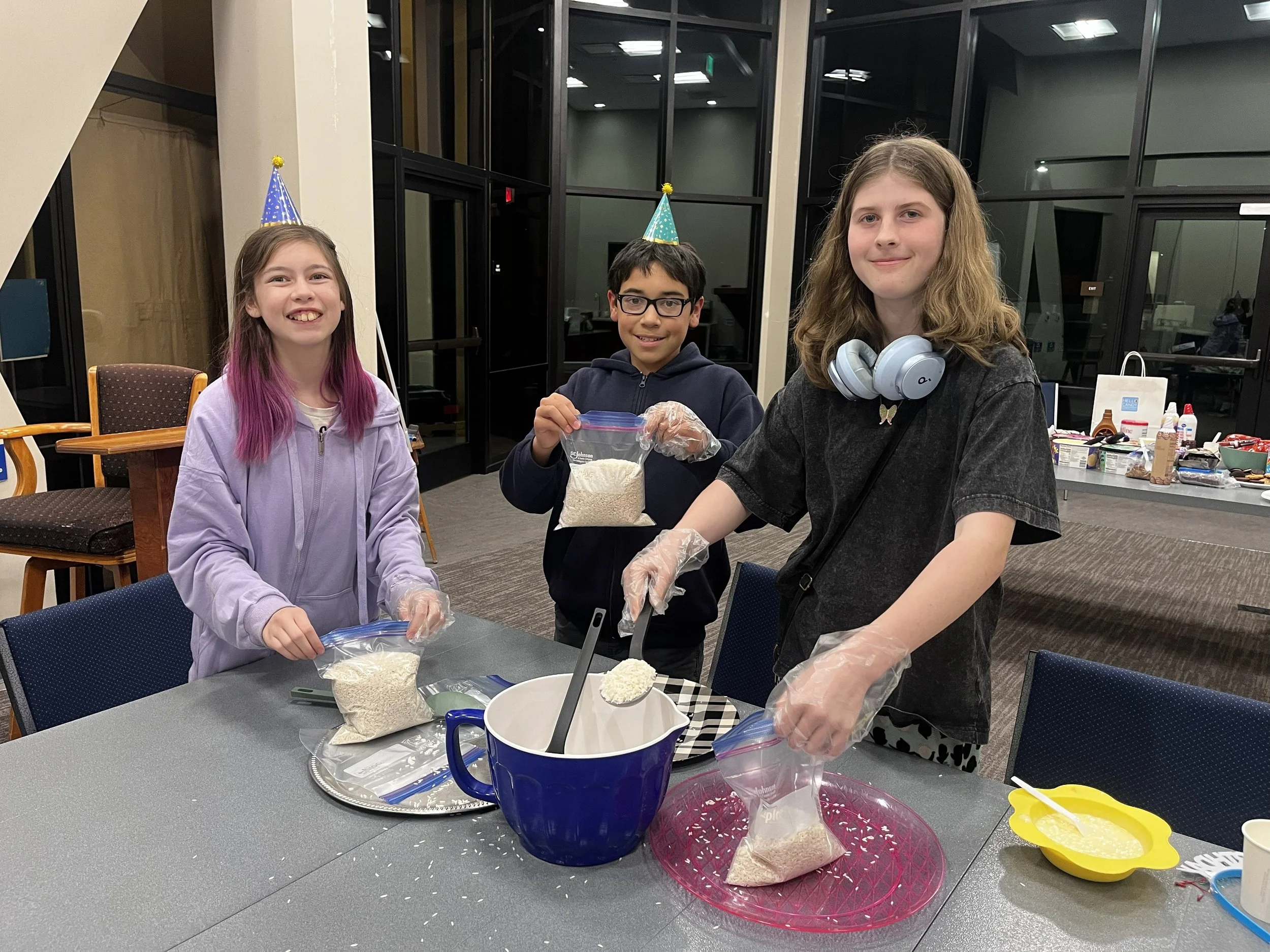 Three teens in party hats portion out dried rice for food distribution  