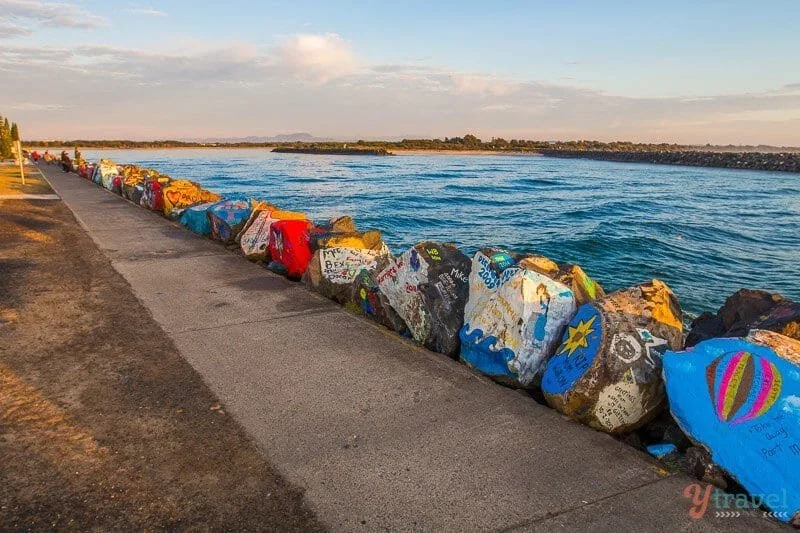 Painted rocks along a waterside path with colorful art and messages at the edge of a body of water.