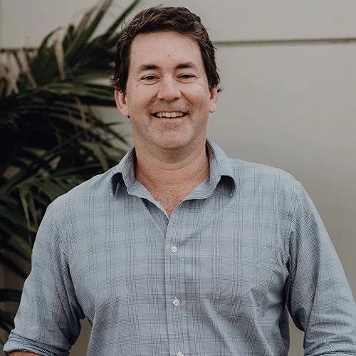 Smiling man in plaid shirt standing in front of a plant