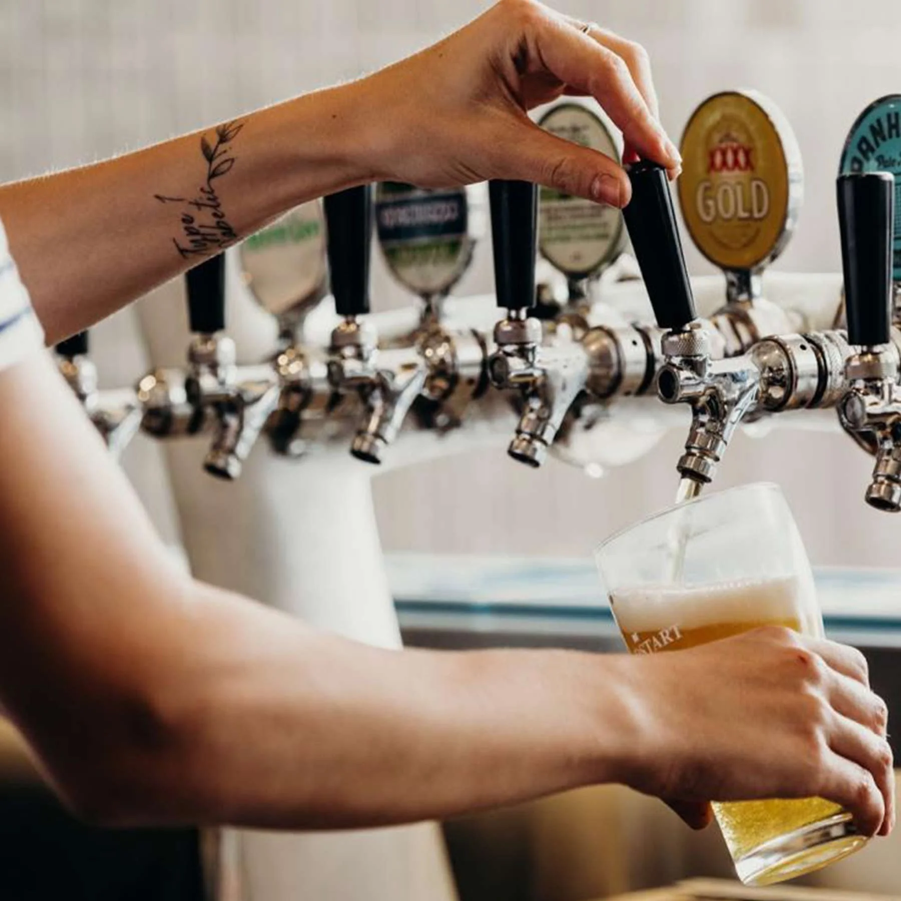 Person pouring draft beer from a tap into a glass at a bar.