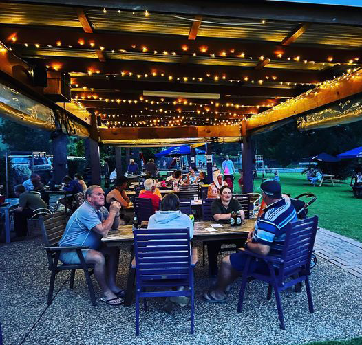 Outdoor dining area with people seated under a pergola adorned with string lights.